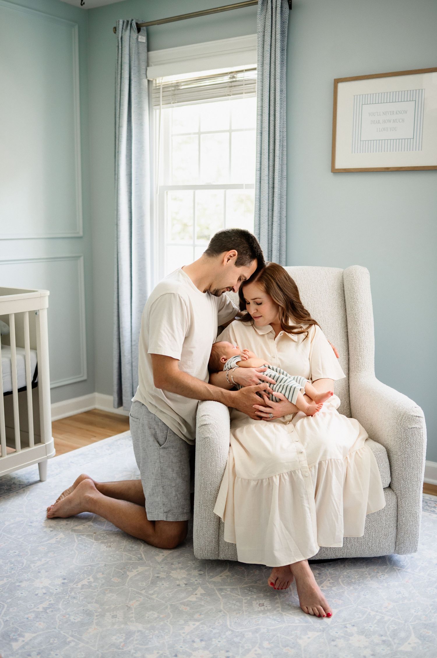 Parents cuddling their newborn baby in a nursery rocking chair during a lifestyle in-home newborn photography session in Raleigh NC