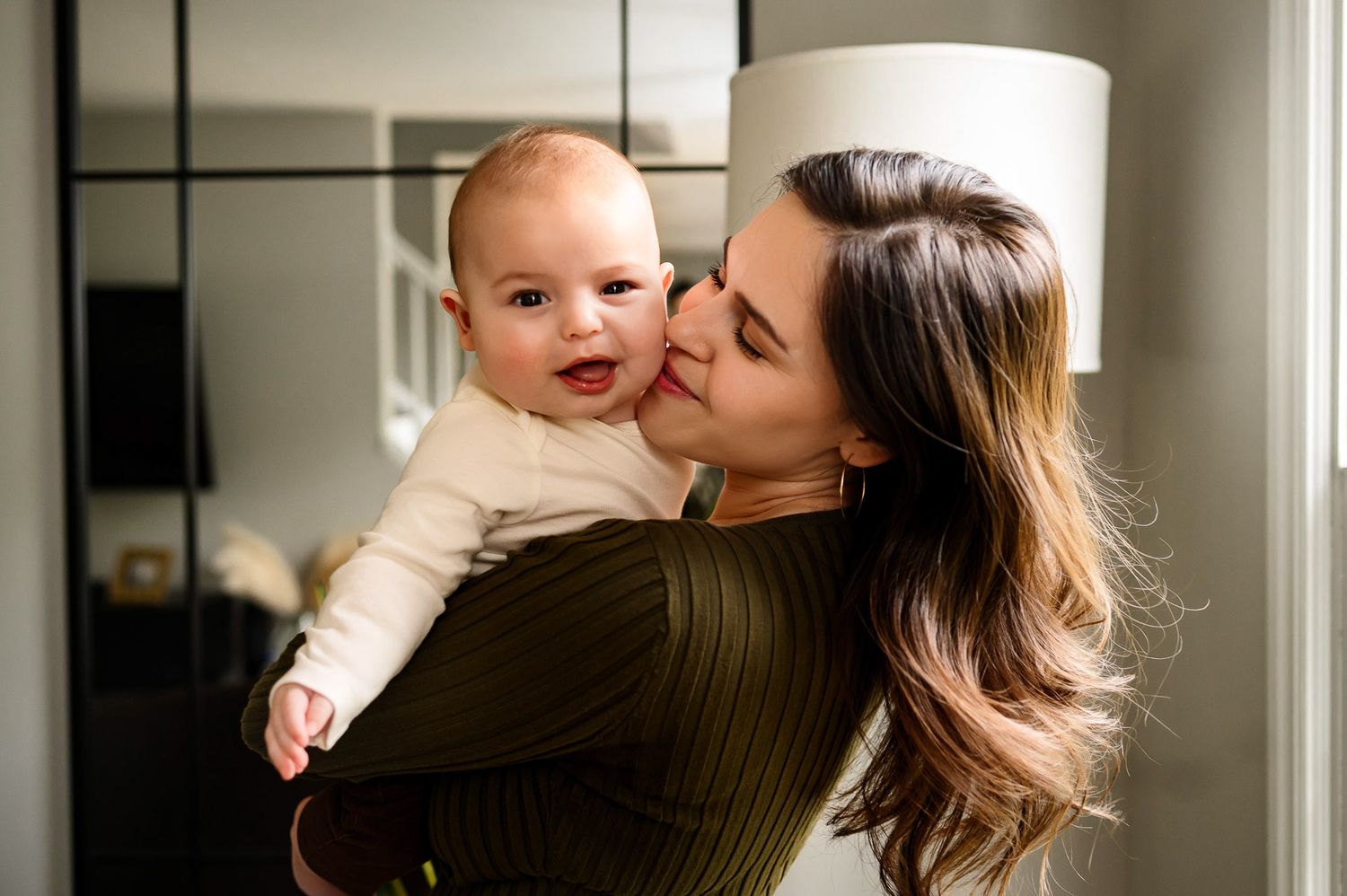 Mother holding her smiling baby during a natural light lifestyle family photography session at home in Raleigh NC