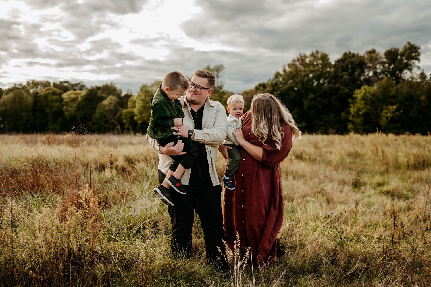 Family of four during a fall family photography session in Raleigh NC with parents holding their two young sons in an open field