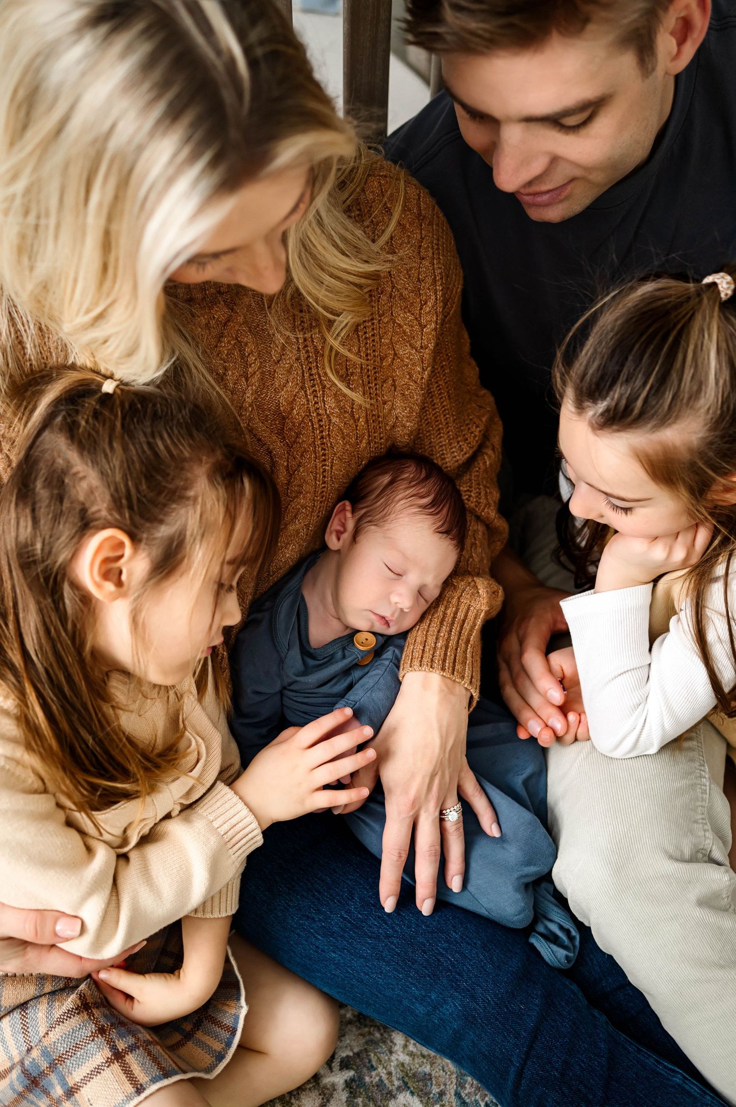 Two sisters gently touching their newborn sibling during a lifestyle newborn photography session in Raleigh NC