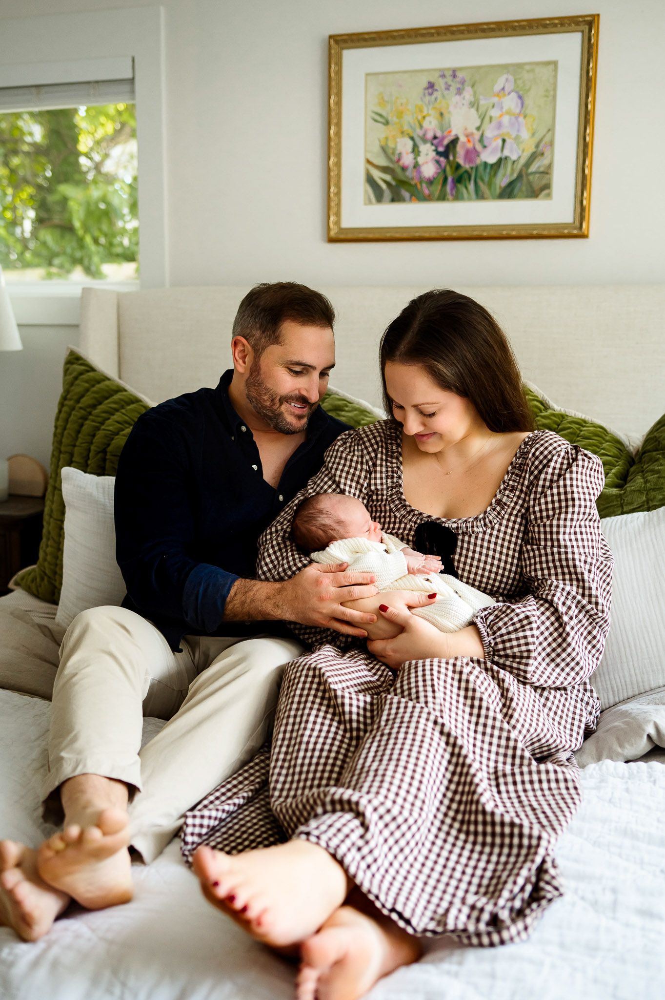 Parents sitting on a bed holding their newborn baby during a cozy in-home newborn photography session in the Triangle area of North Carolina