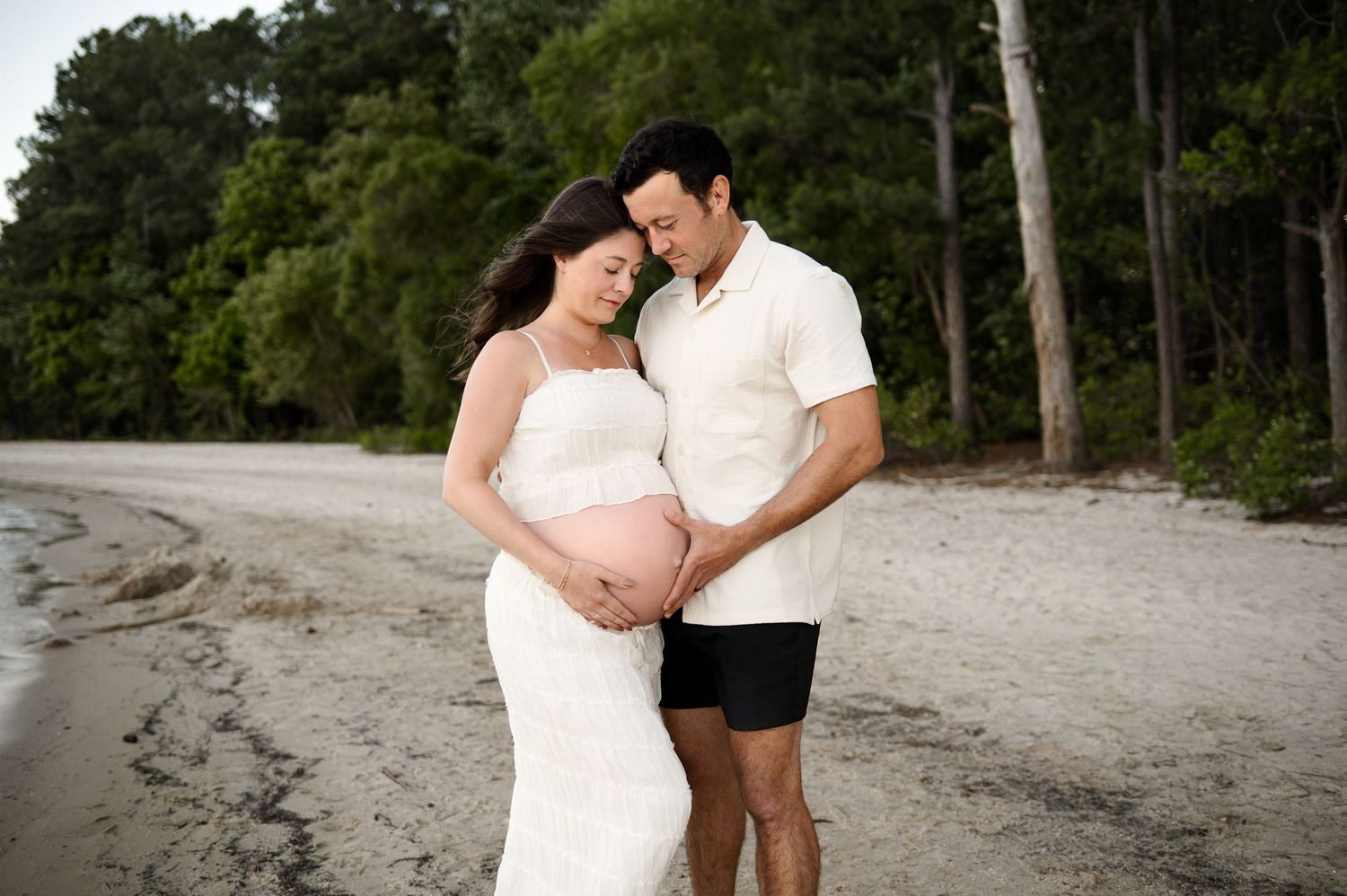 A Raleigh family photographer captures expecting couple standing together admiring mother's growing belly