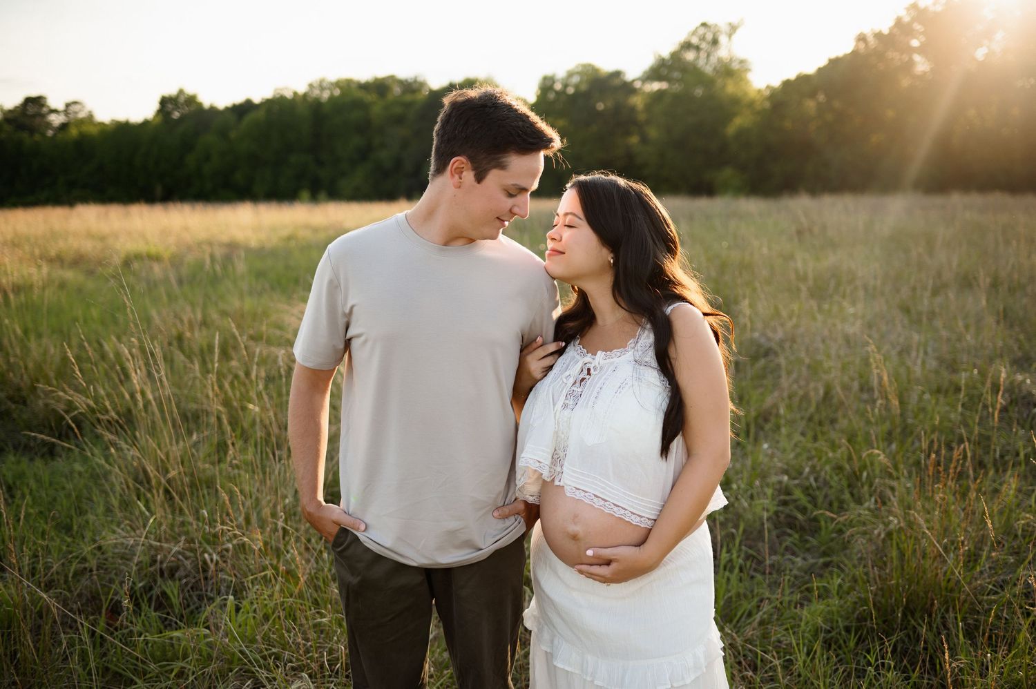 Mother resting her chin on father's shoulder while holding her exposed pregnant belly during a Raleigh maternity photography session