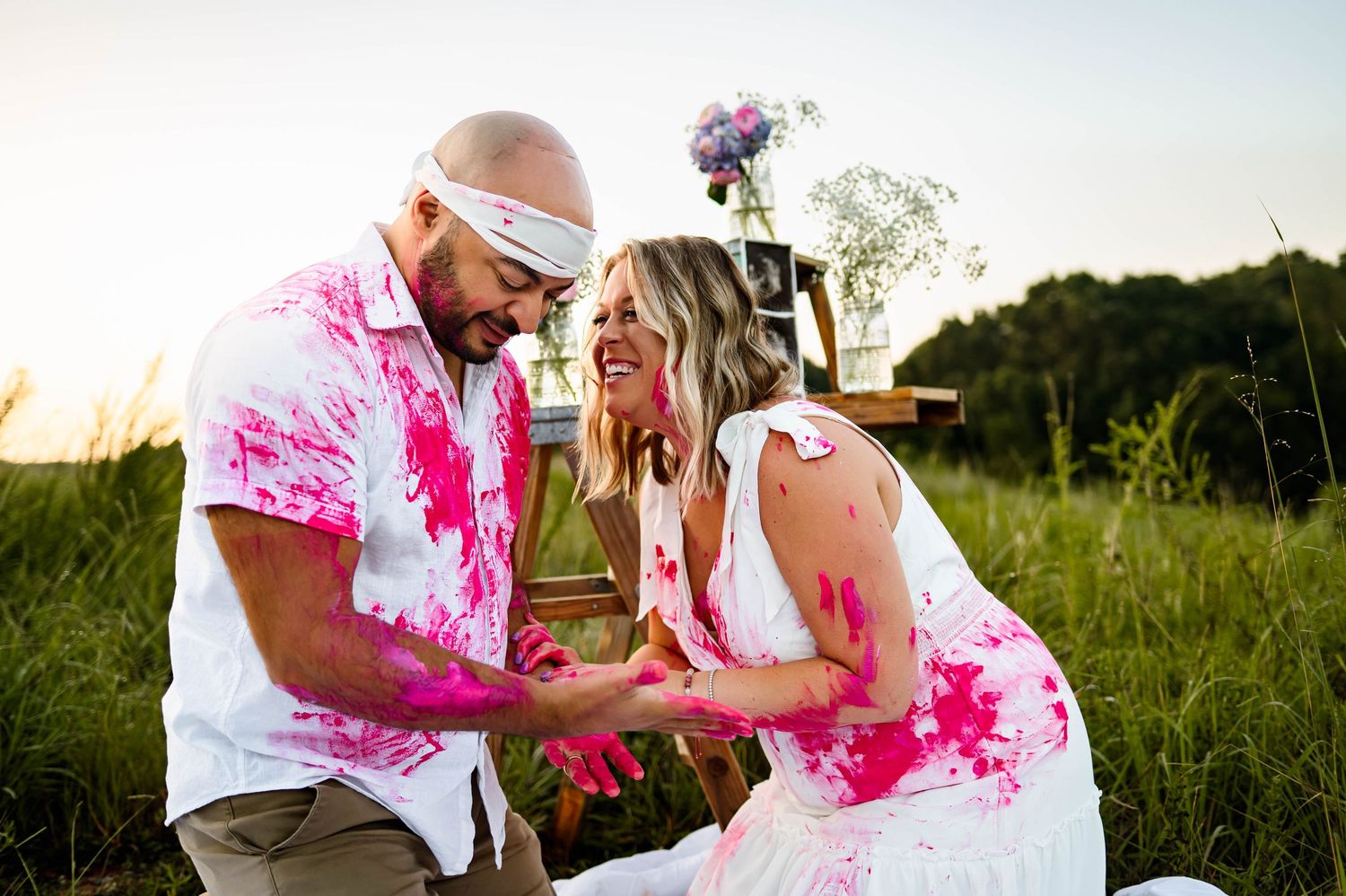 Candid moment of expecting parents laughing together during a Raleigh gender reveal photography session filled with pink paint and emotion