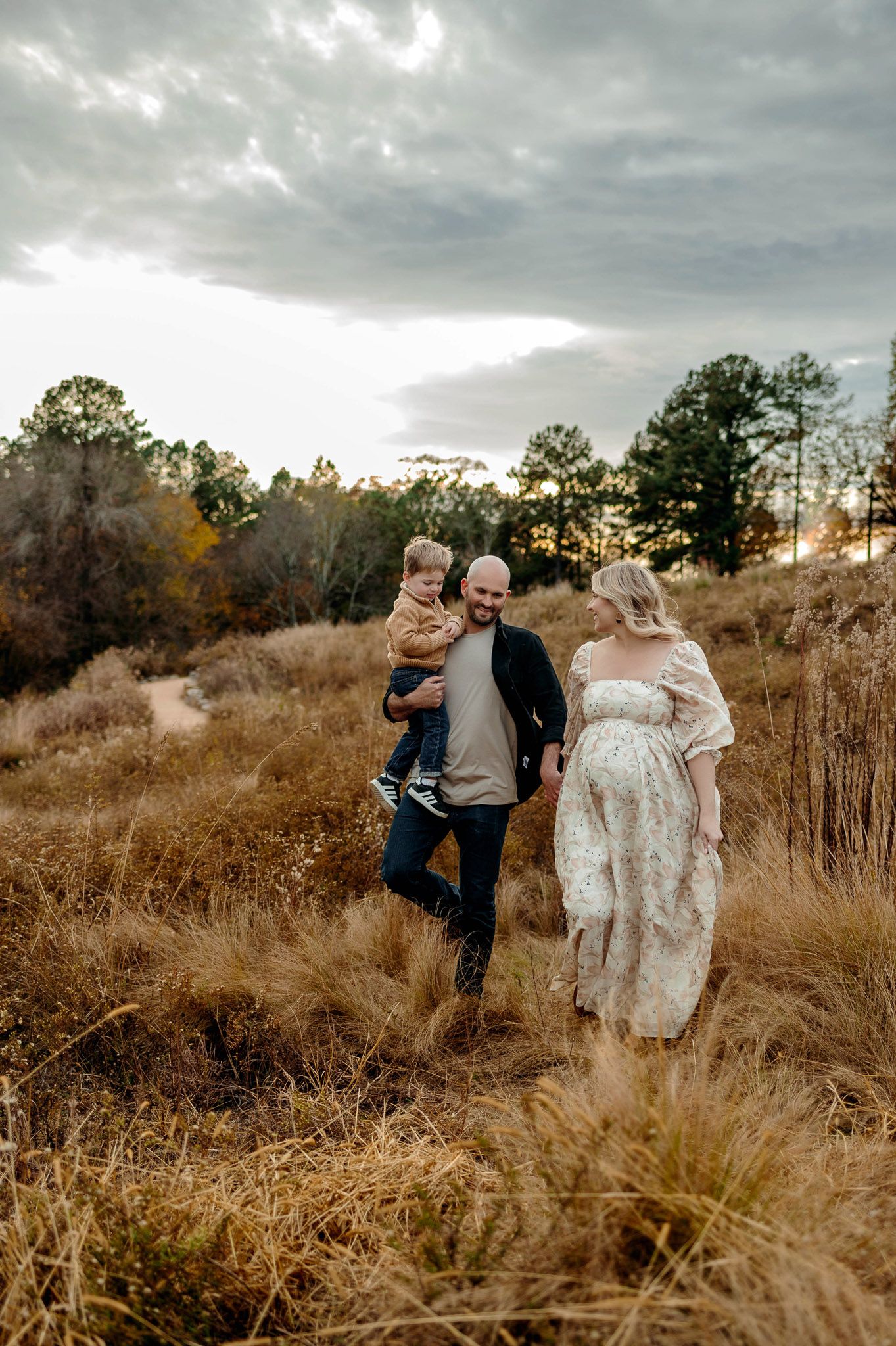 Expectant parents walking through a natural field with their young son during an outdoor maternity photography session