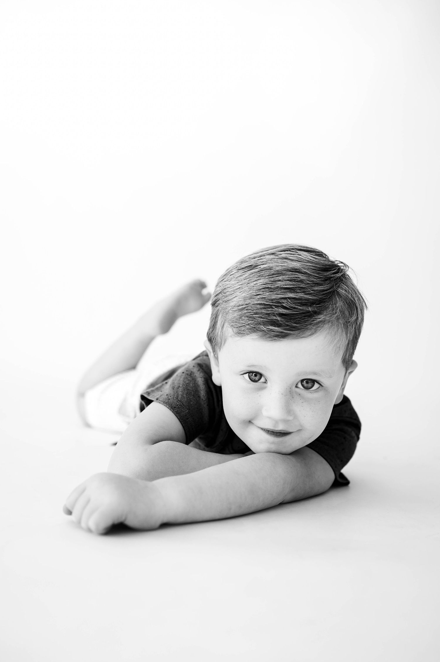 A black and white photo series showing a young child in various playful reclining poses on a white background with Apex family photographer