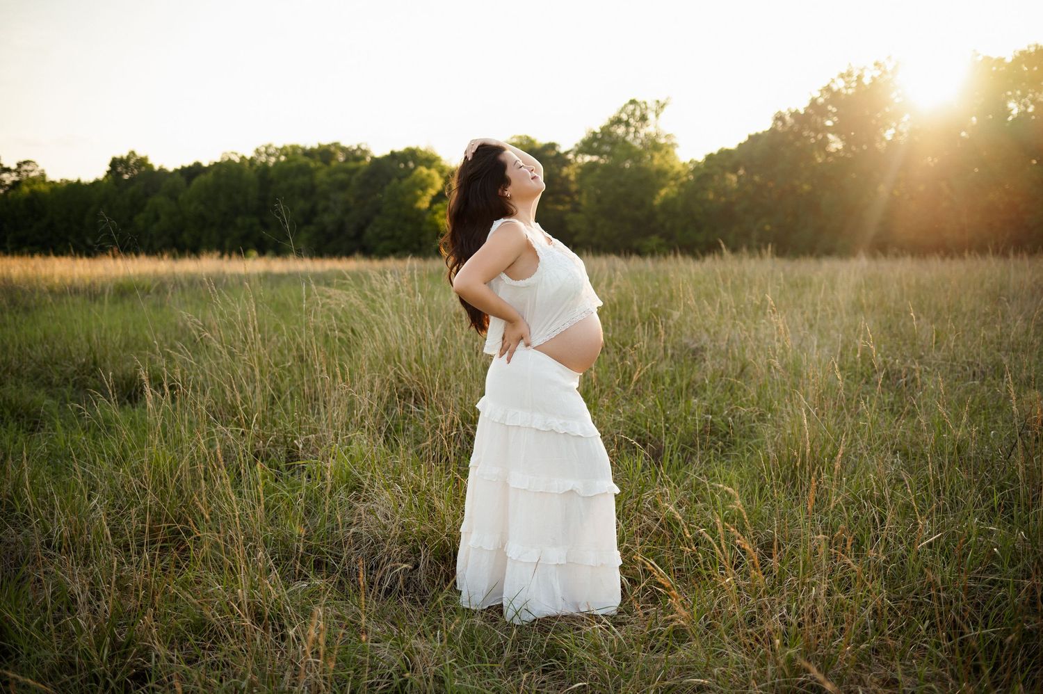 Raleigh maternity photographer captures an expecting mother standing alone in a sunlit field playing with her hair