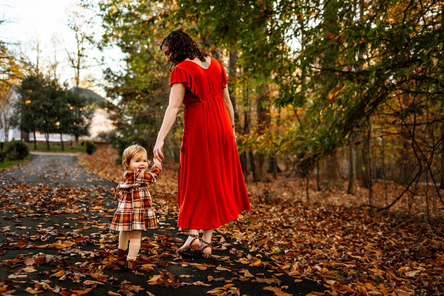 Mother and daughter in red dresses hold hands while walking on a sunlit path during a family photography session durham nc