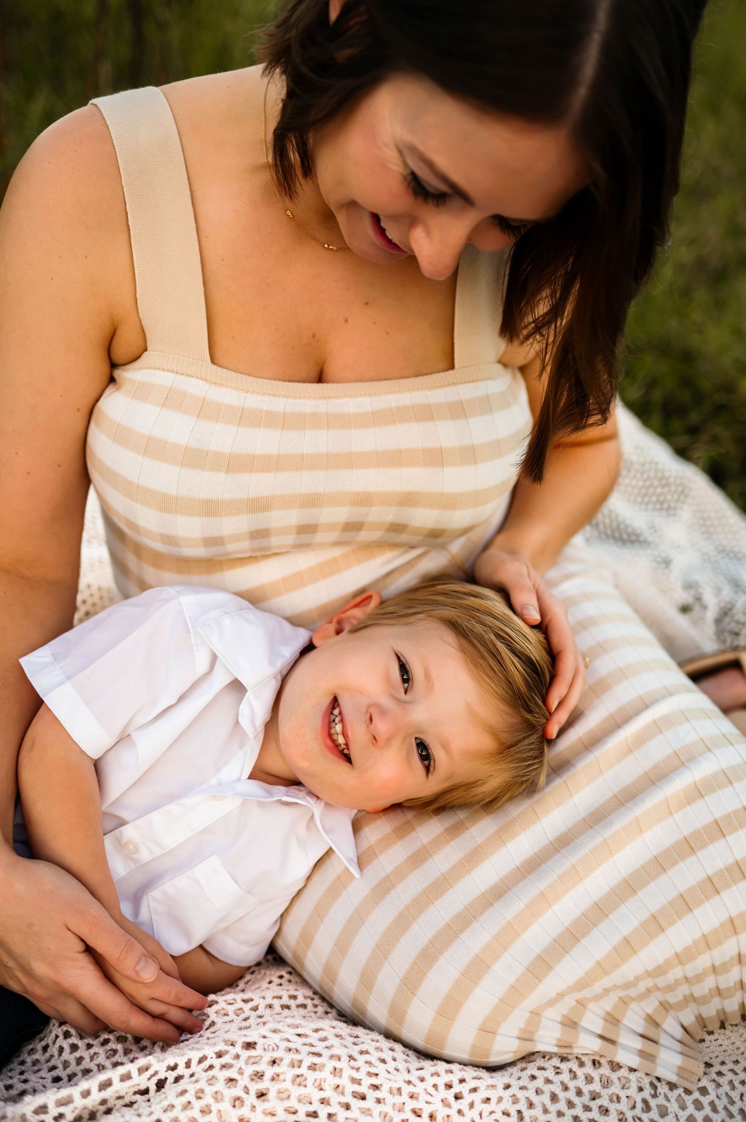 A tender moment captured outdoors showing affection and joy while relaxing on a blanket in sunlit grass with Emma Branch Photography