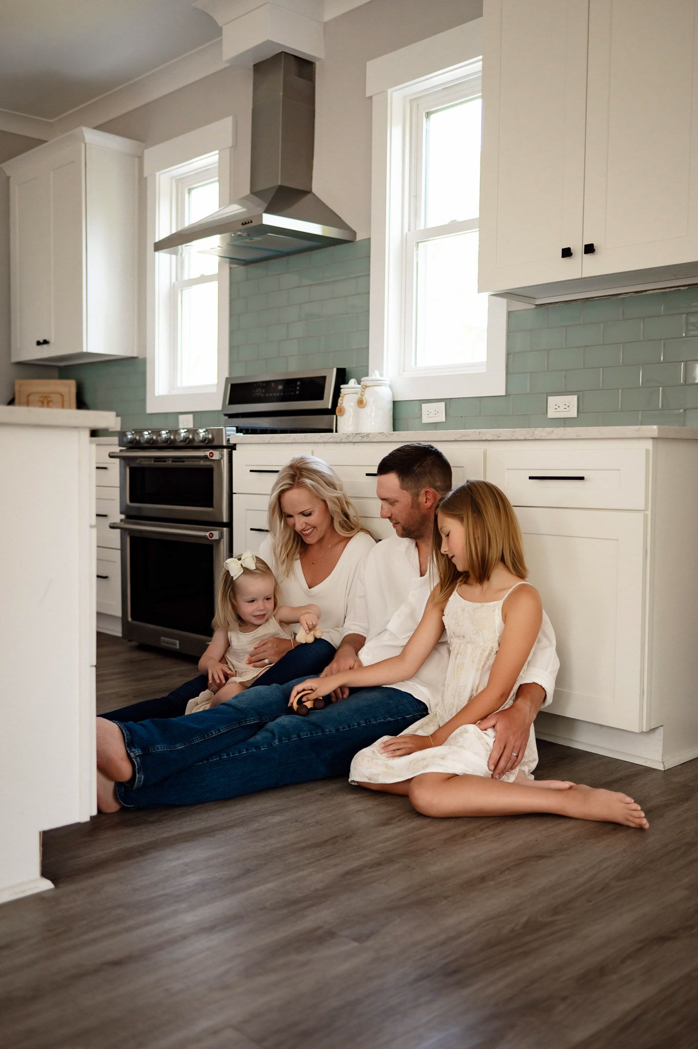 Parents sitting on the kitchen floor with their daughters during a natural in-home family photography session near Durham NC