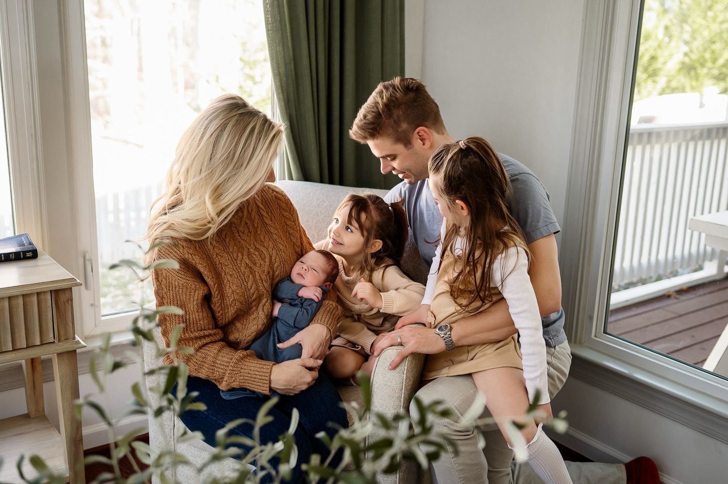 Parents and two young daughters gathered together with their newborn baby during a lifestyle newborn photography session at home