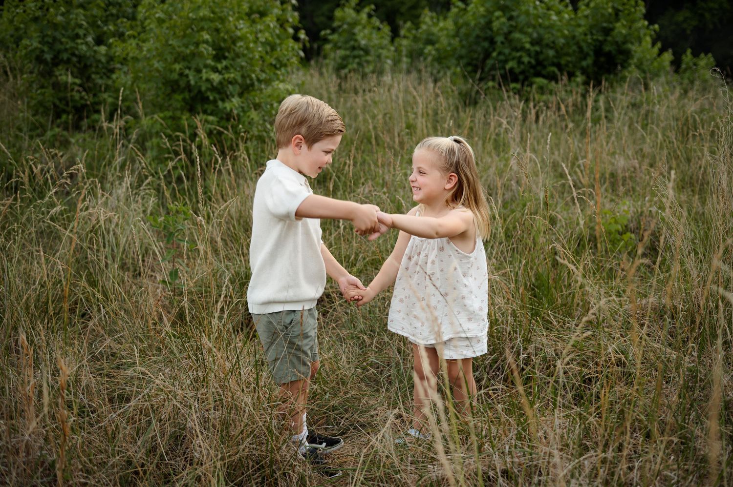 Two siblings holding hands and playing together in a grassy field during a Raleigh family photography session