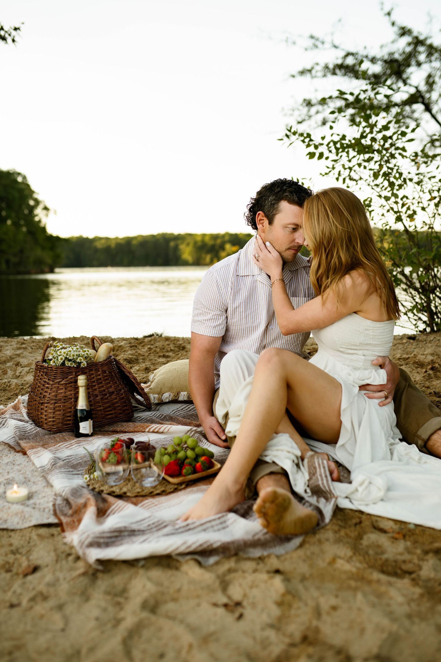 A romantic beach picnic scene with a couple sharing intimate moments on a blanket with wine and food during family photography session