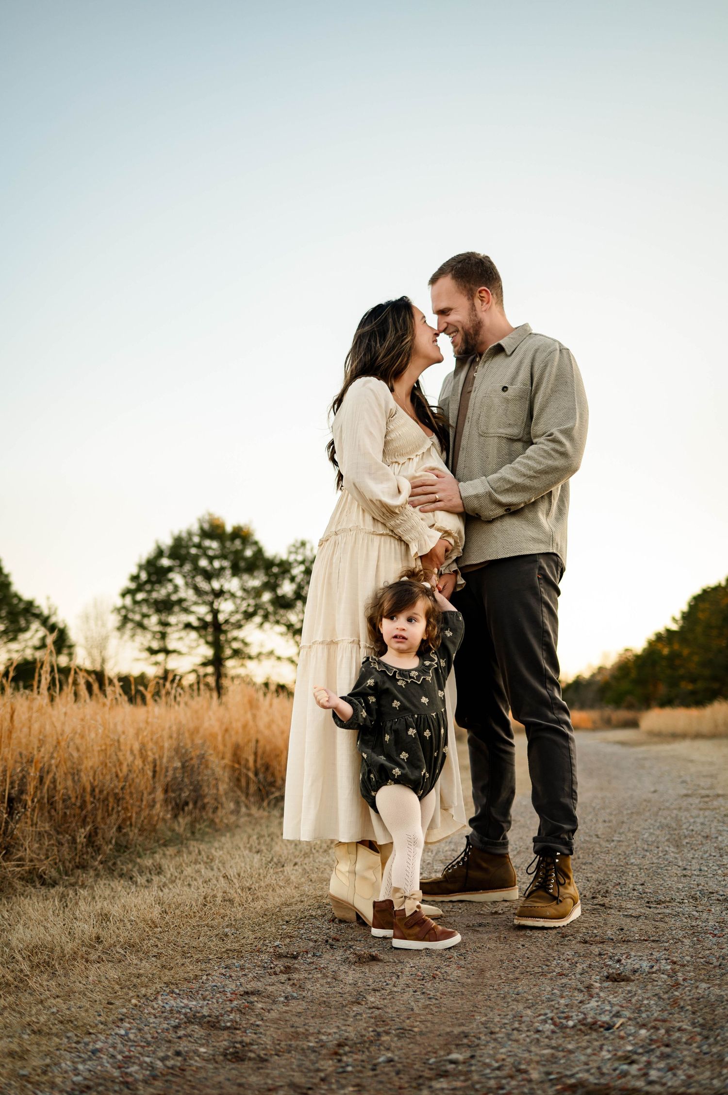 Family standing together on dirt path at sunset with golden field and trees during family maternity photography session in Apex NC