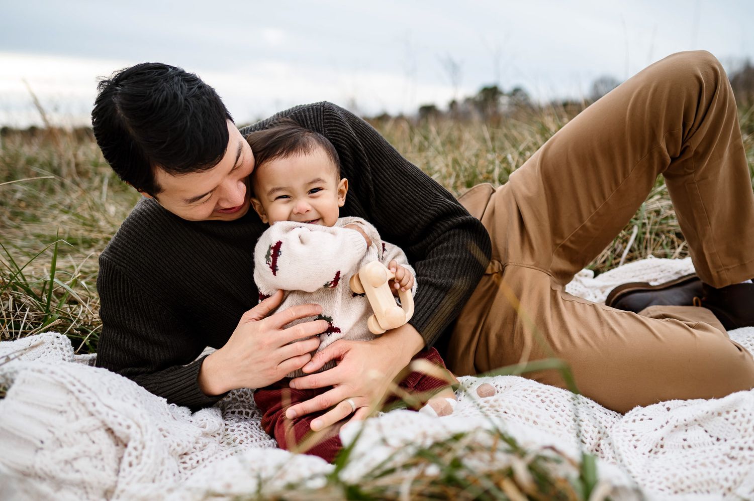 Father lying on a blanket and cuddling his baby during a relaxed outdoor family photography session in Raleigh NC