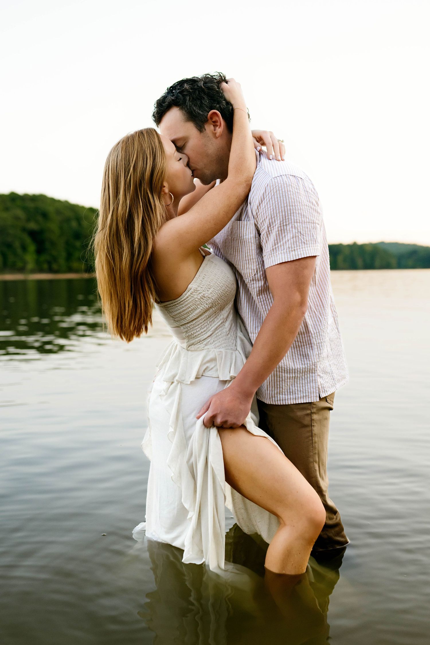 Romantic couple embraces by a serene lake during sunset, creating an intimate silhouette against the water in Raleigh NC