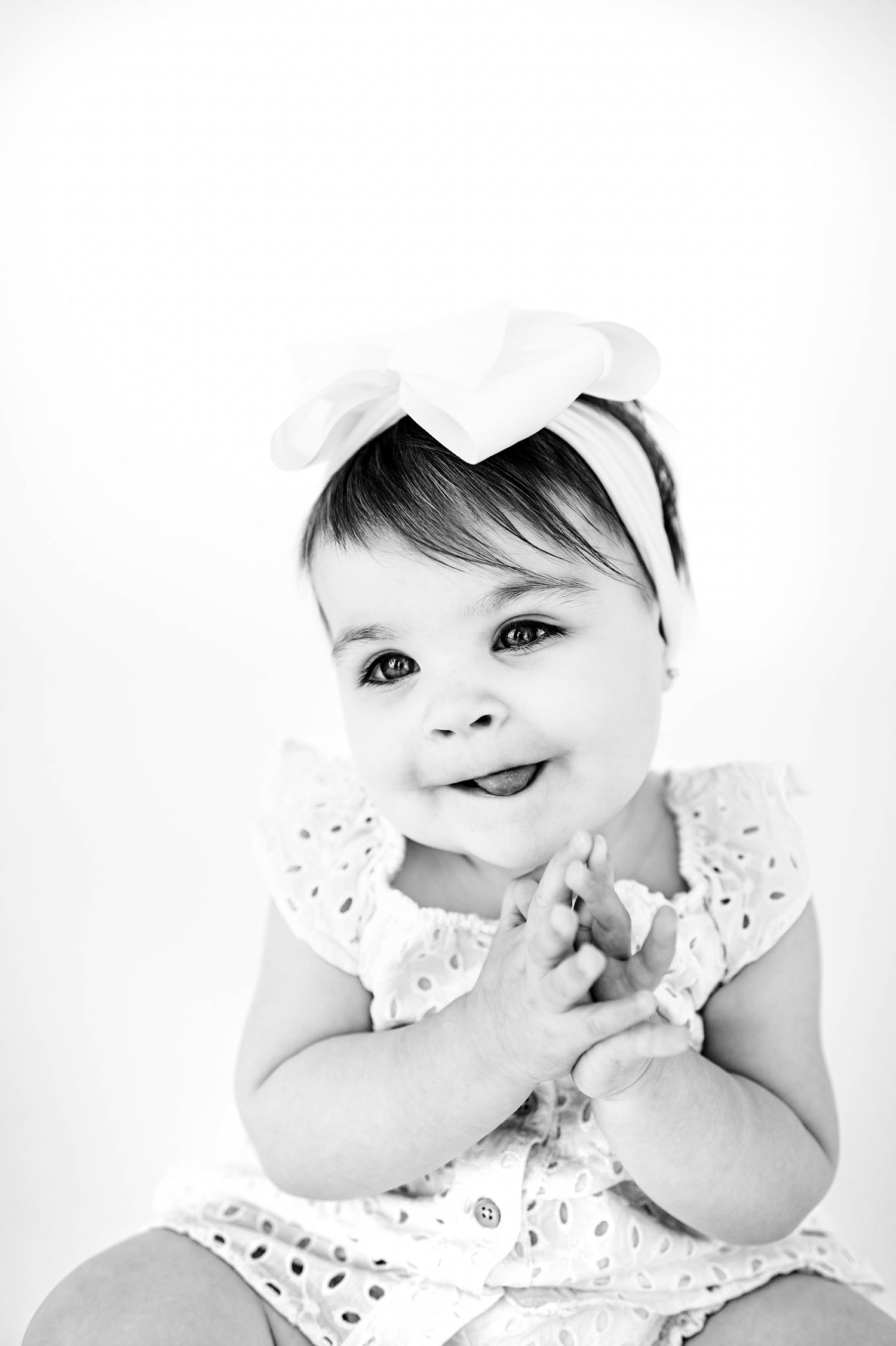 Black and white portrait of a smiling baby wearing a white headband and polka dot dress during childhood personality mini session in Raleigh