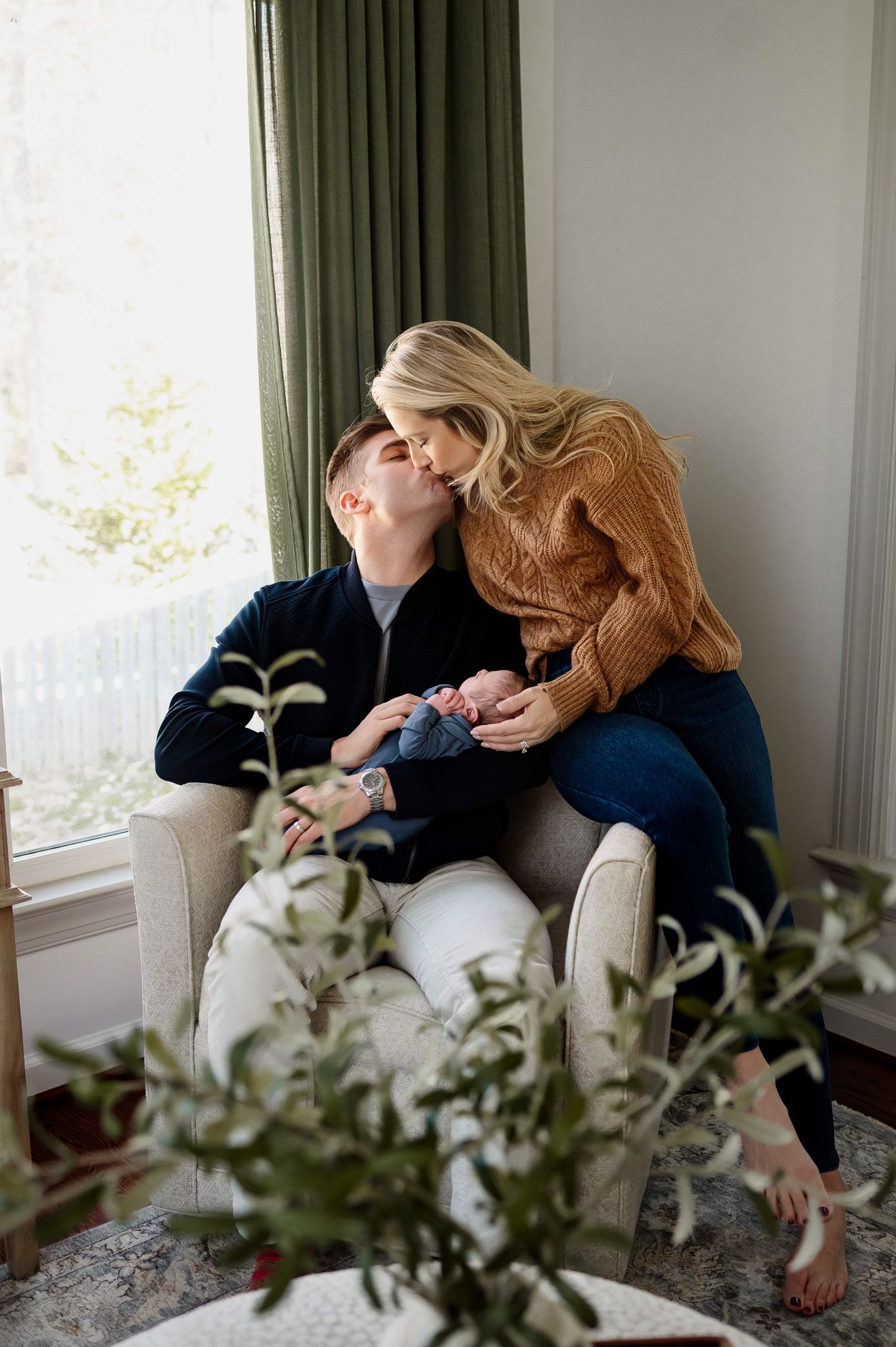Parents sharing a kiss while holding their newborn baby during a cozy in-home newborn photography session