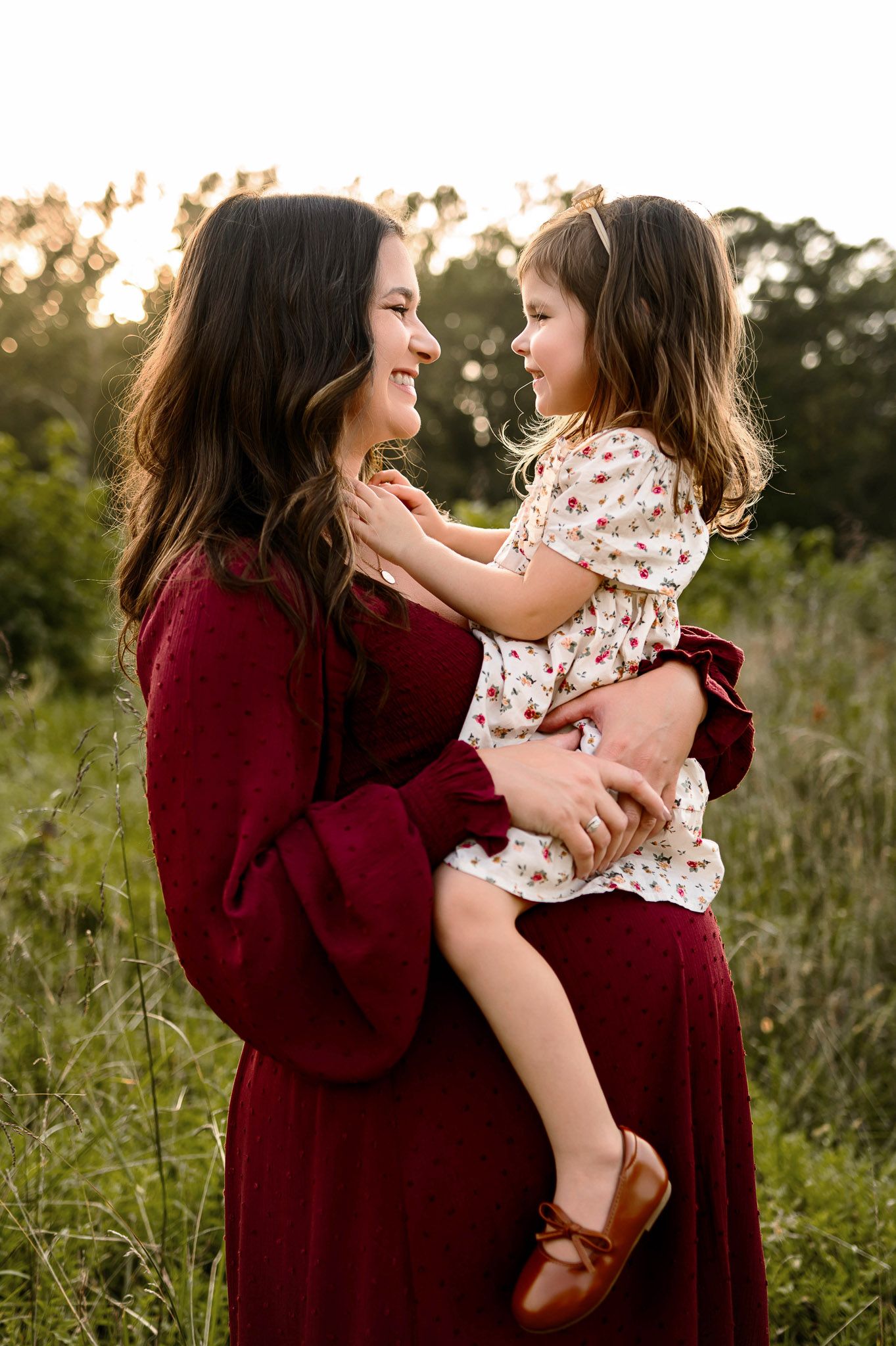 Mother holding her young daughter during outdoor maternity photography session in a natural field setting