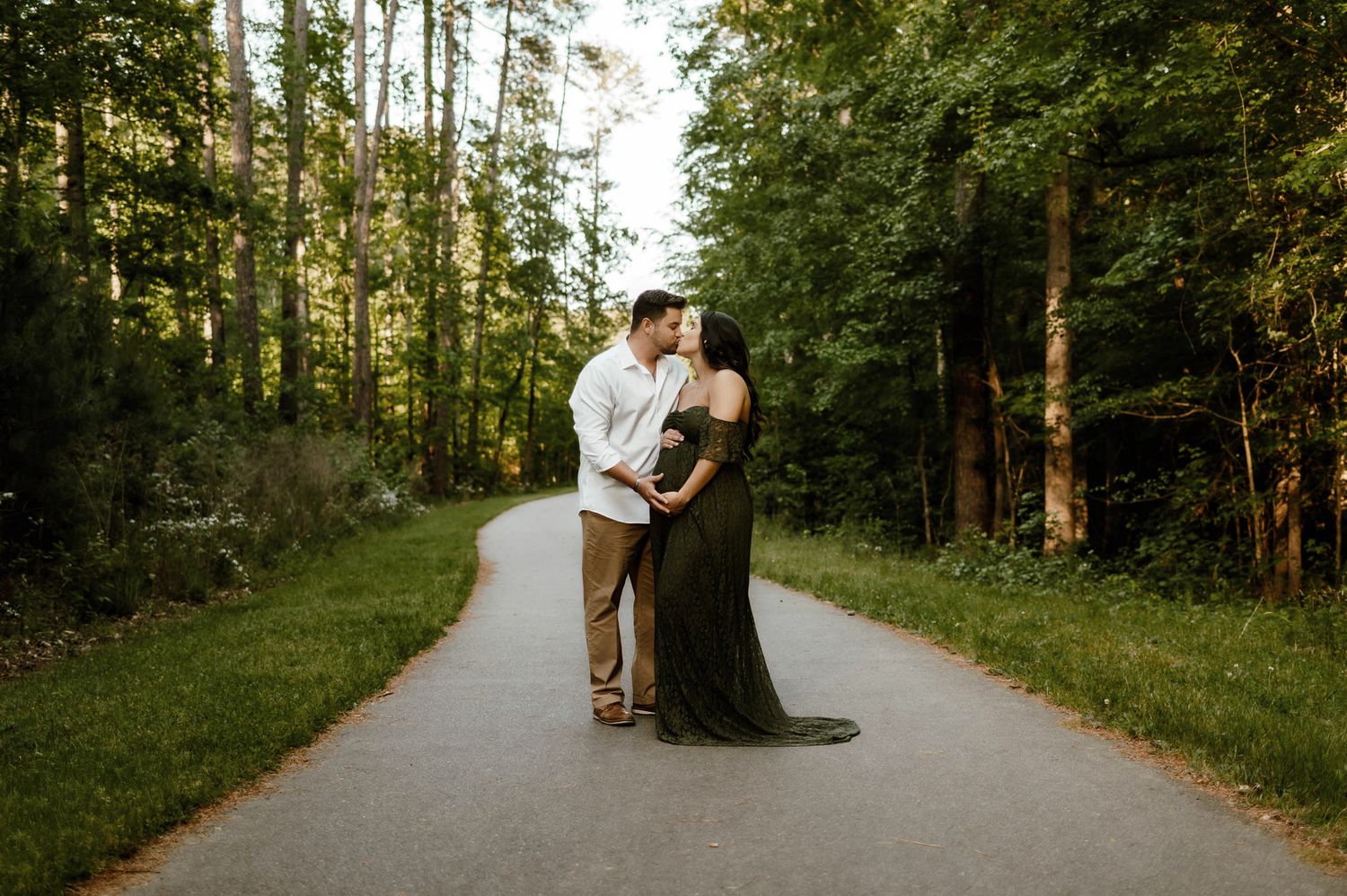 Expectant couple kissing while standing on a wooded trail during a Raleigh maternity photography session
