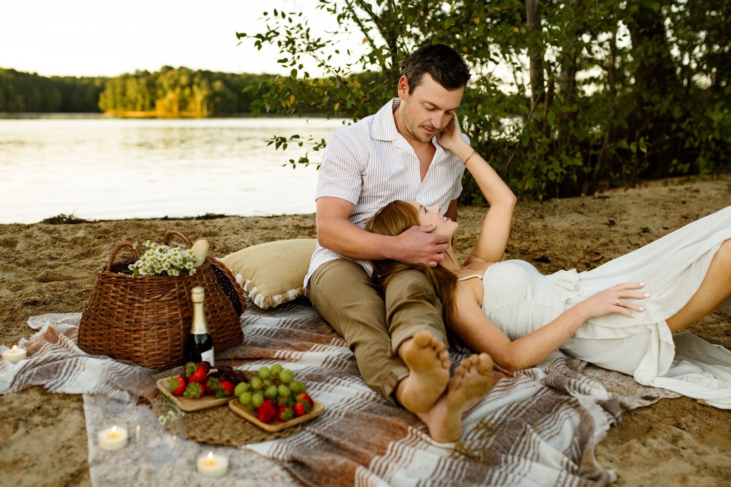 Couple enjoying a romantic beach picnic with wine and snacks on a blanket at sunset with Raleigh family photographer