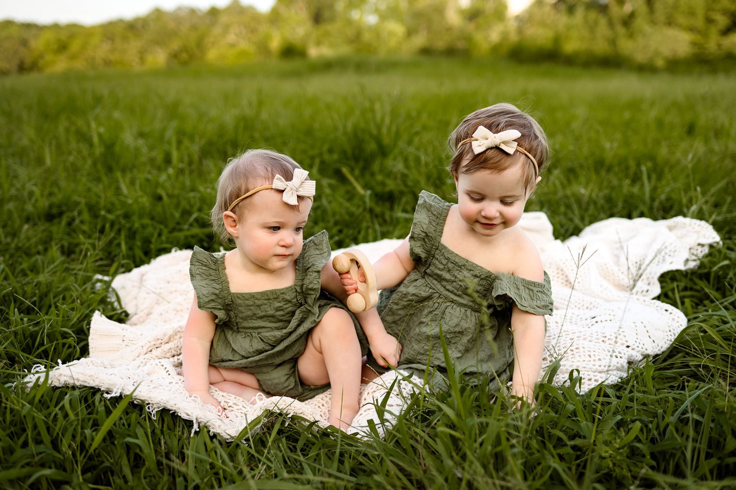 Twin baby girls sitting in grass on knit blanket during outdoor family photography session in Apex NC