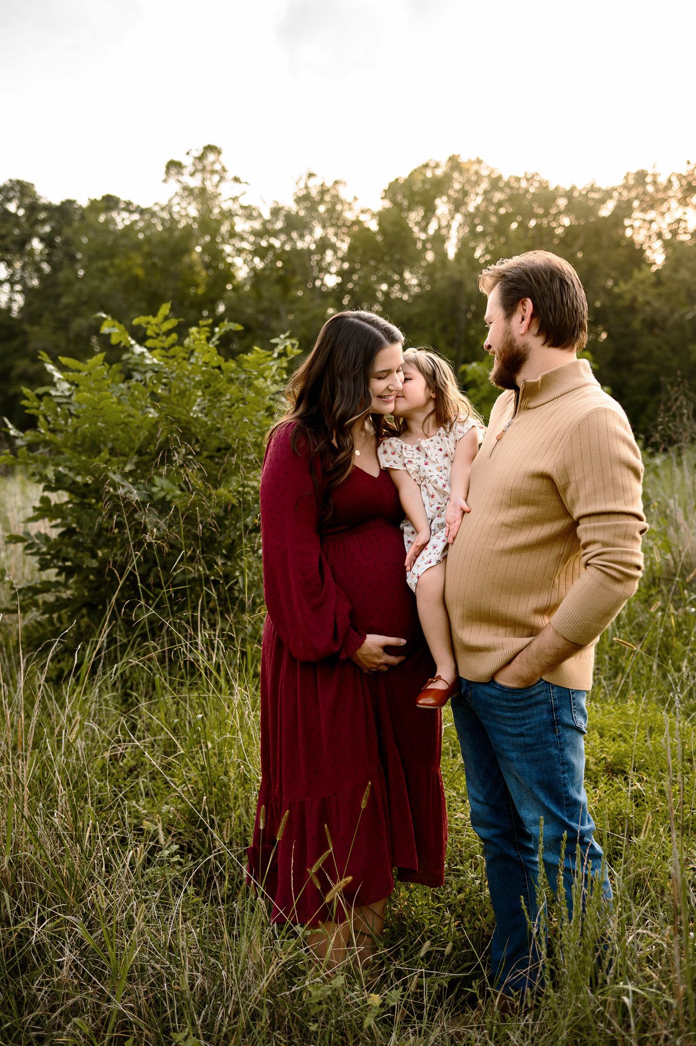 Outdoor maternity family photography session with parents and young daughter sharing a moment in Wake Forest NC