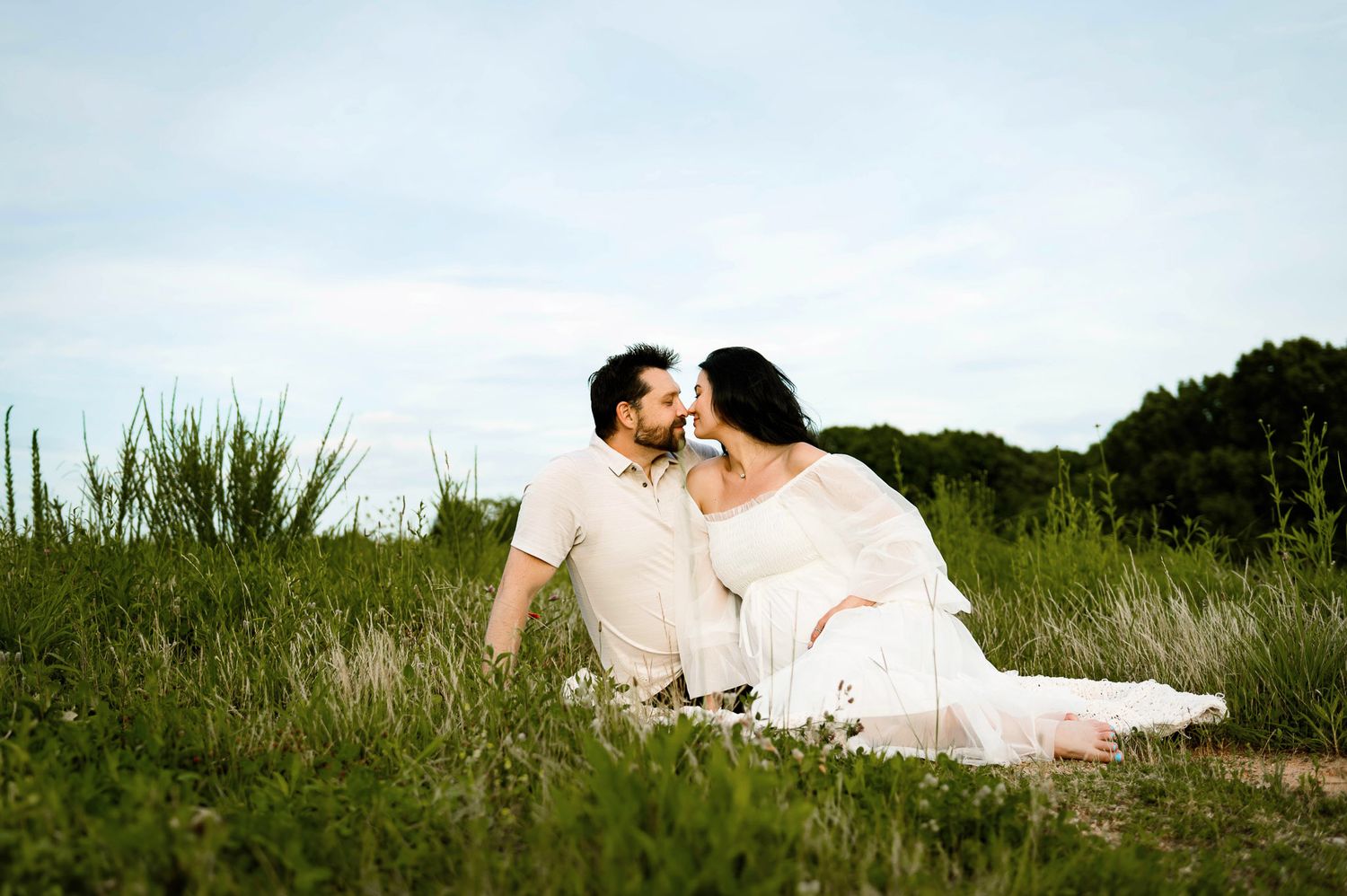 Expectant couple sitting together in a field during a Raleigh maternity photography session