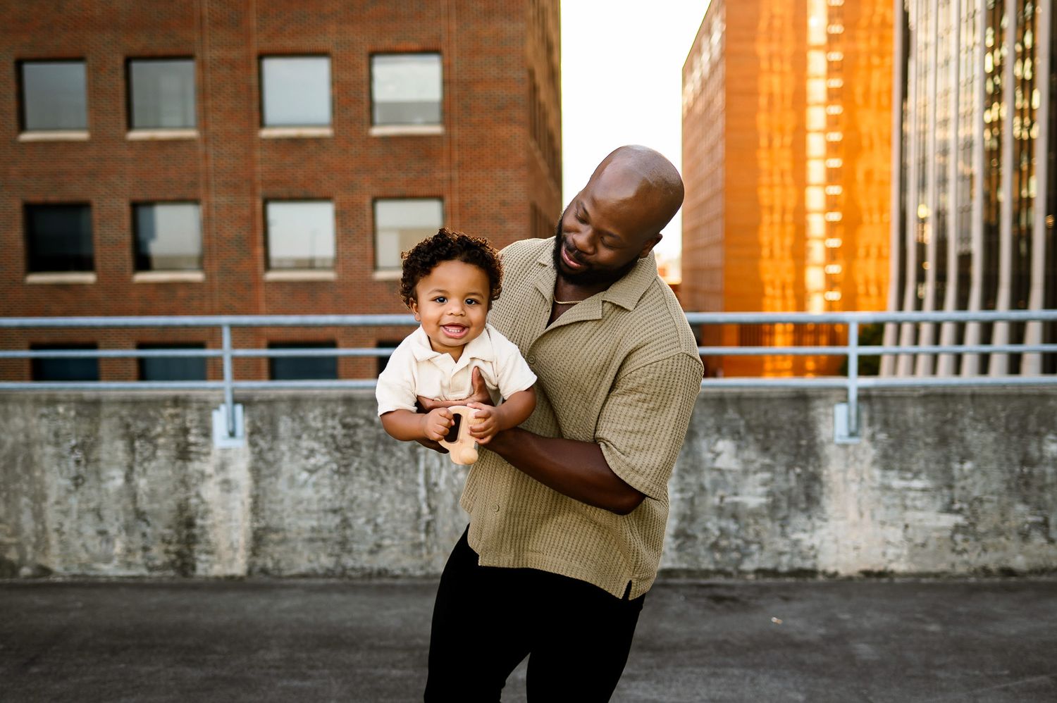 Father holding his toddler during an urban family photography session with downtown Raleigh buildings in the background