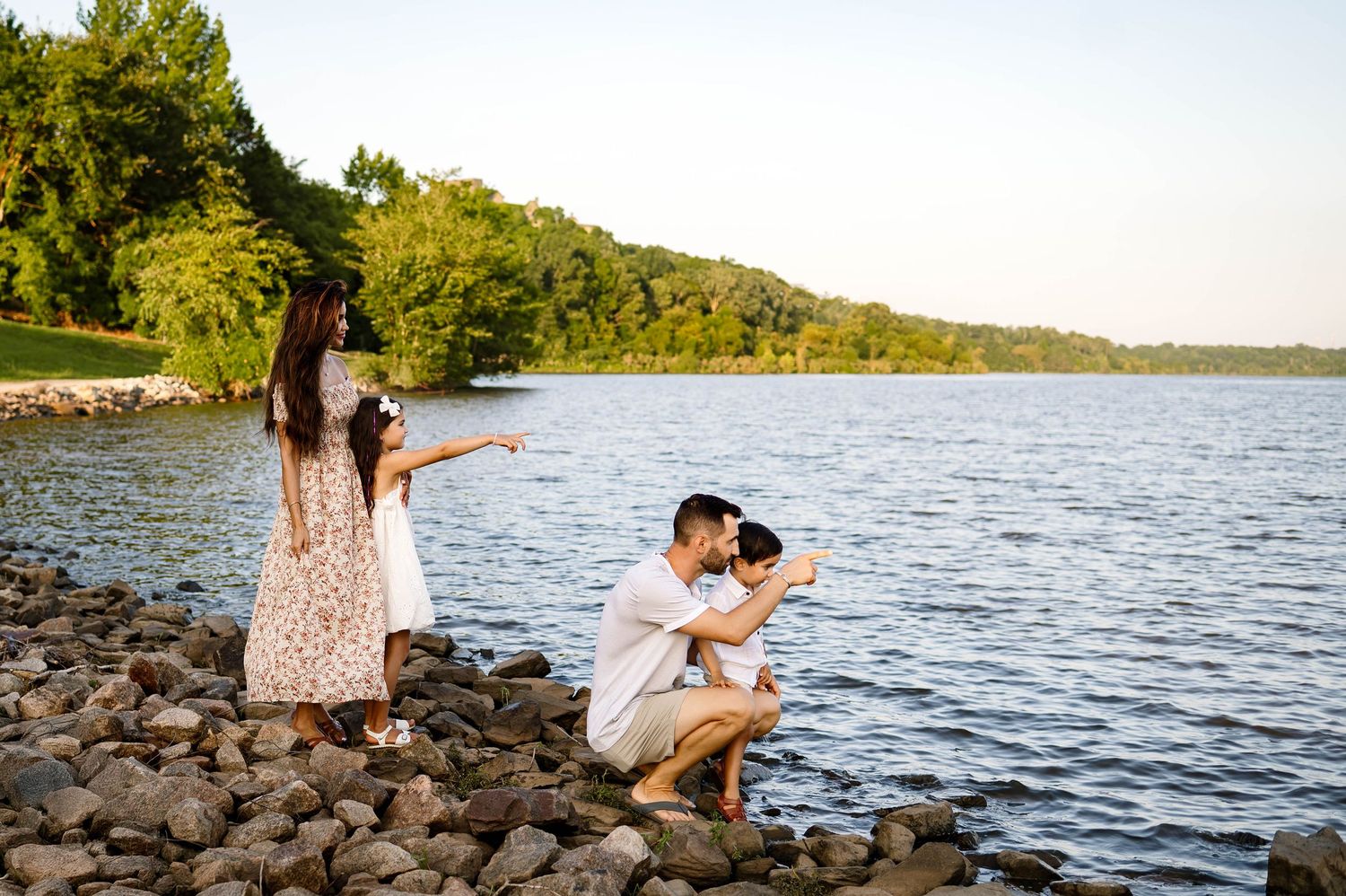 Family standing by the lake pointing toward the water during a sunrise natural light photo session with Raleigh family photographer