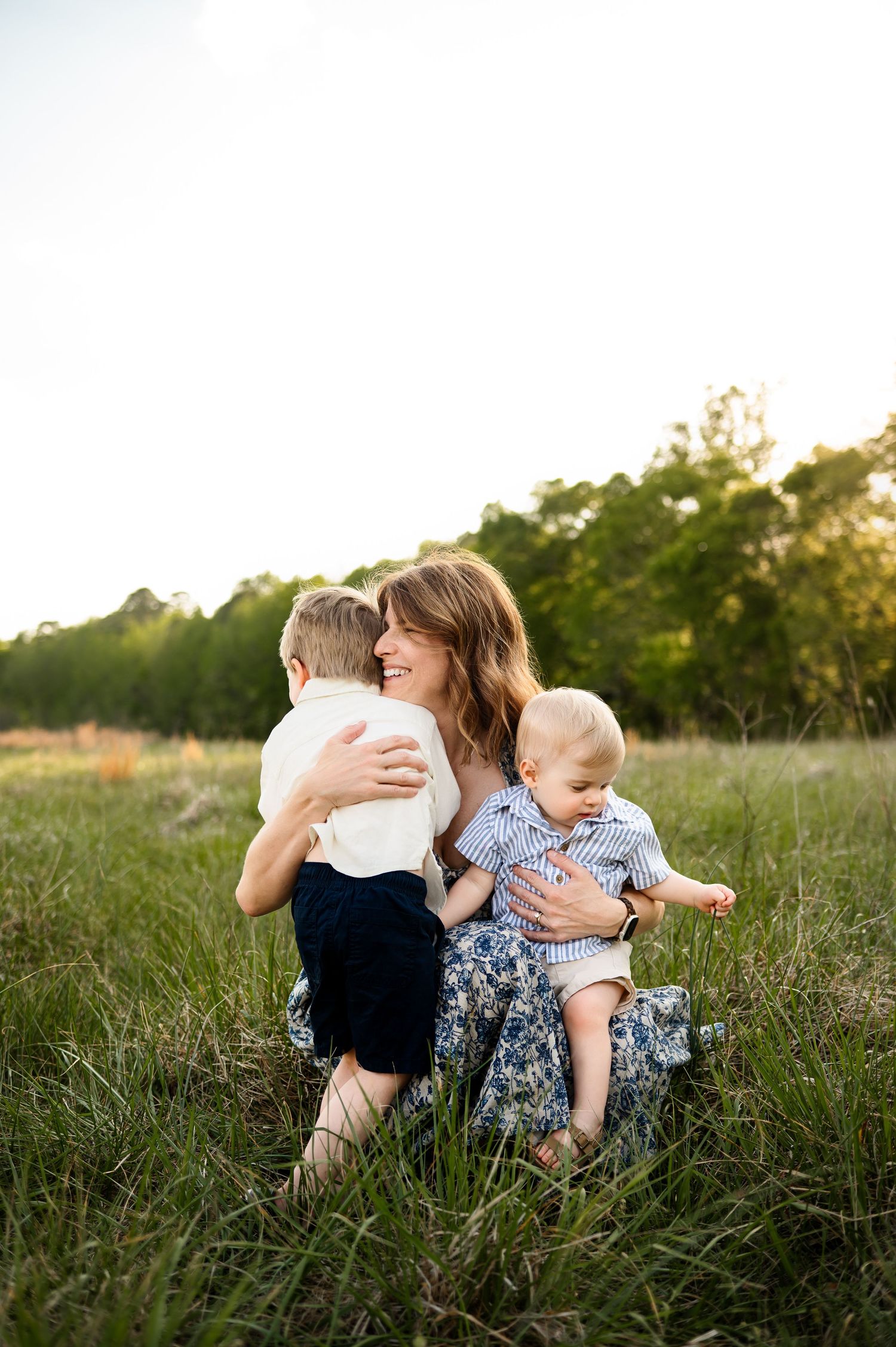 Mother hugging two young children in open field during relaxed family photography session in Raleigh NC