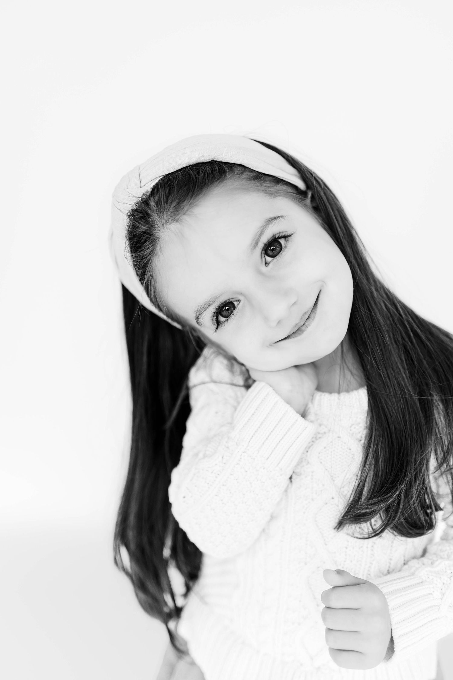 Black and white portrait of a child in a white sweater wearing a headband while smiling at camera with Durham NC newborn photographer