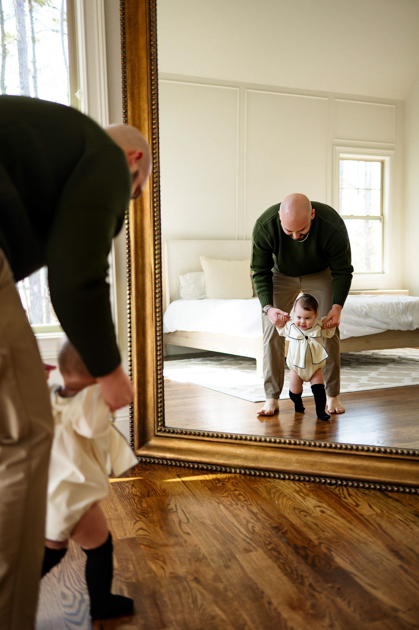 Father helping his baby take steps in a bedroom during a natural in-home family photography session