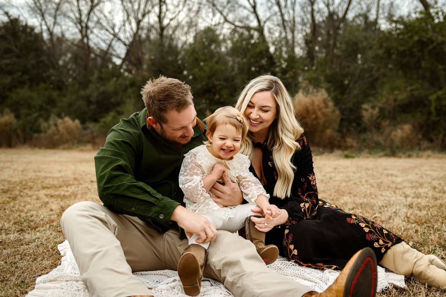 Parents laughing with their toddler while sitting together on a blanket during an outdoor family photography session