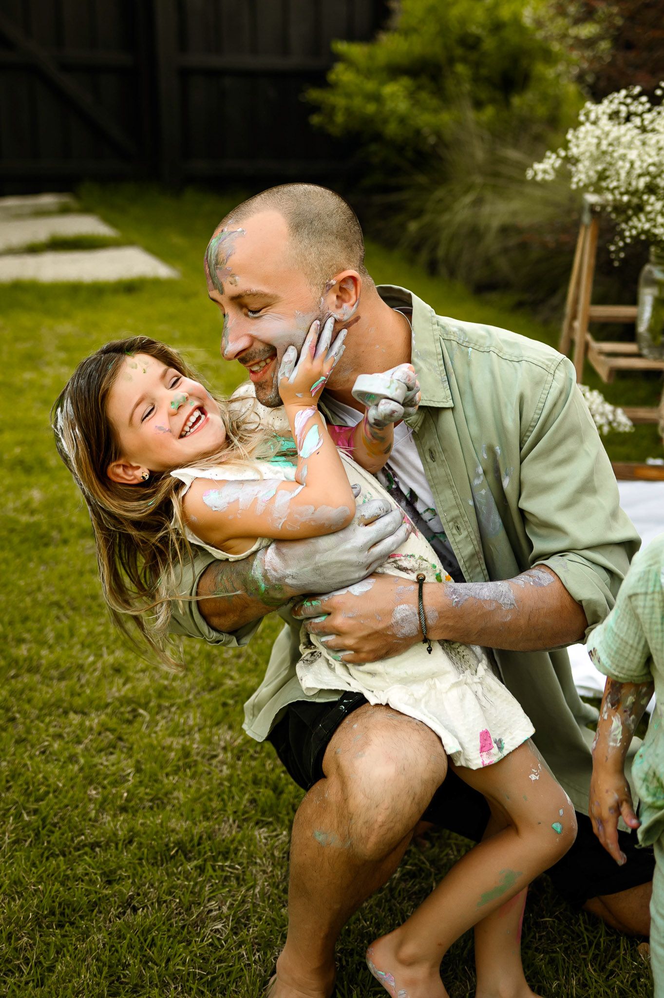 Father laughing while holding his paint-covered daughter during a playful outdoor family photography session