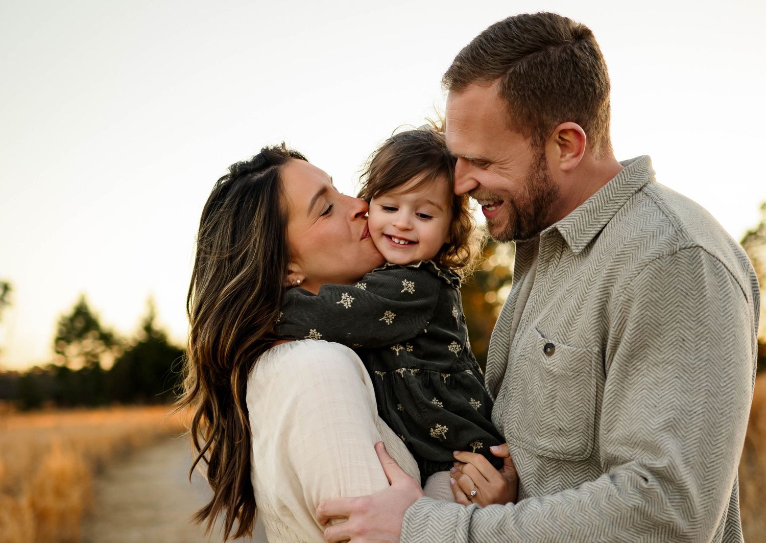 A family shares a joyful moment together outdoors during golden hour in a field for maternity photography session with family raleigh nc