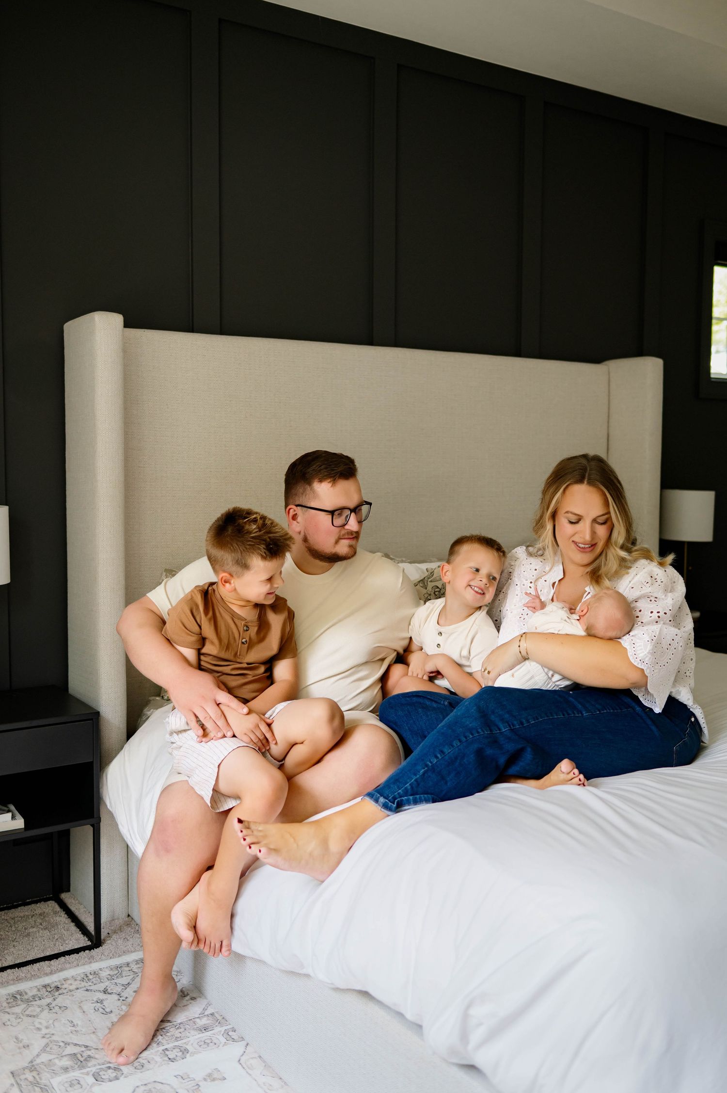 Family of five cuddled together on a bed during a Raleigh in-home newborn photography session captured by Emma Branch