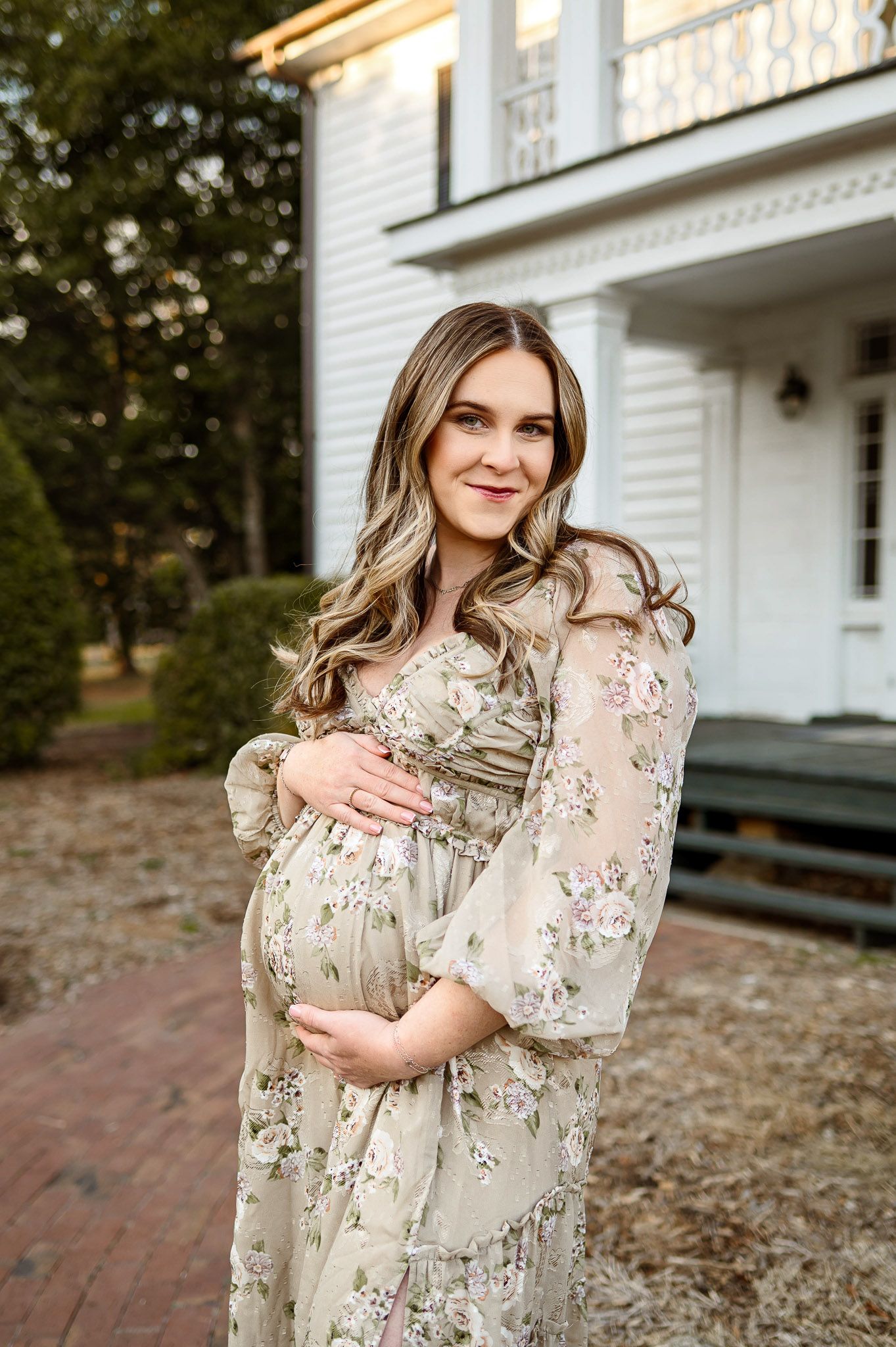 Raleigh maternity photographer capturing a pregnant mother in a floral dress standing outside a historic home