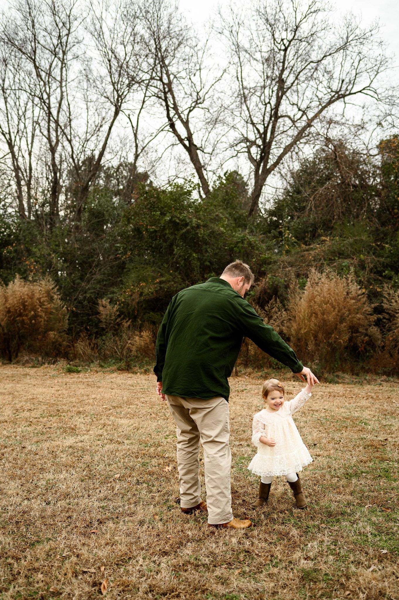 Father spinning his daughter in a grassy field during a playful family photography session outdoors in Raleigh NC