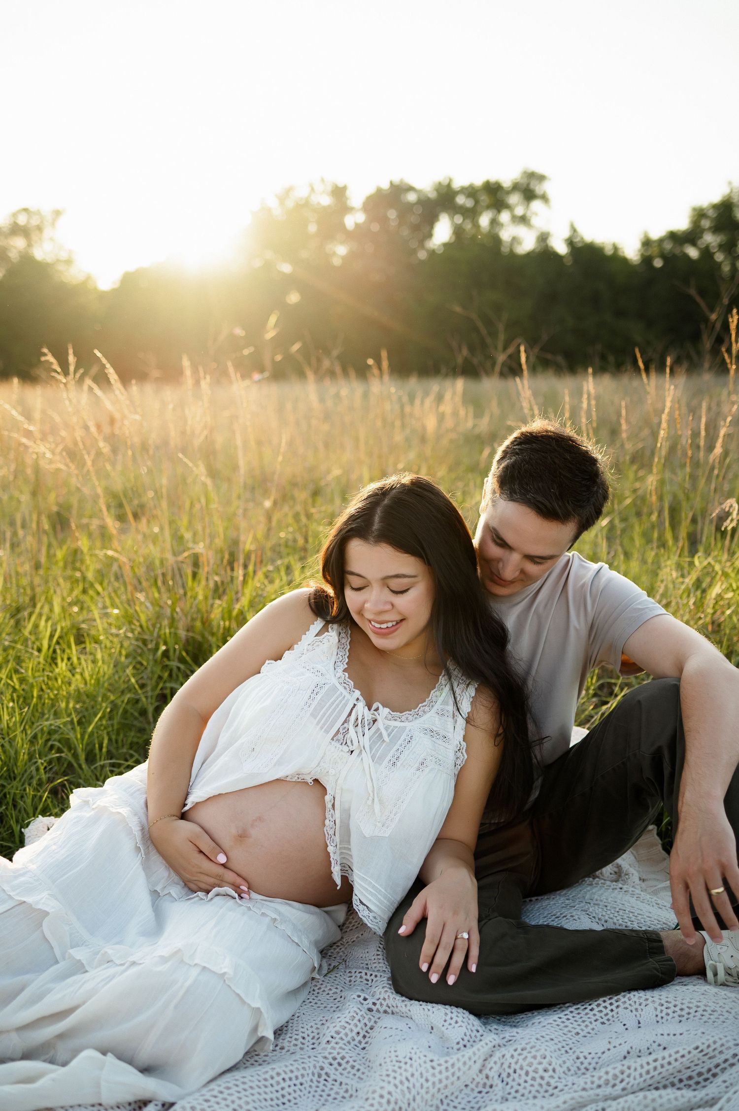 Expecting parents sit together in a grassy field during golden hour in Wake Forest for a maternity photography session with Emma Branch