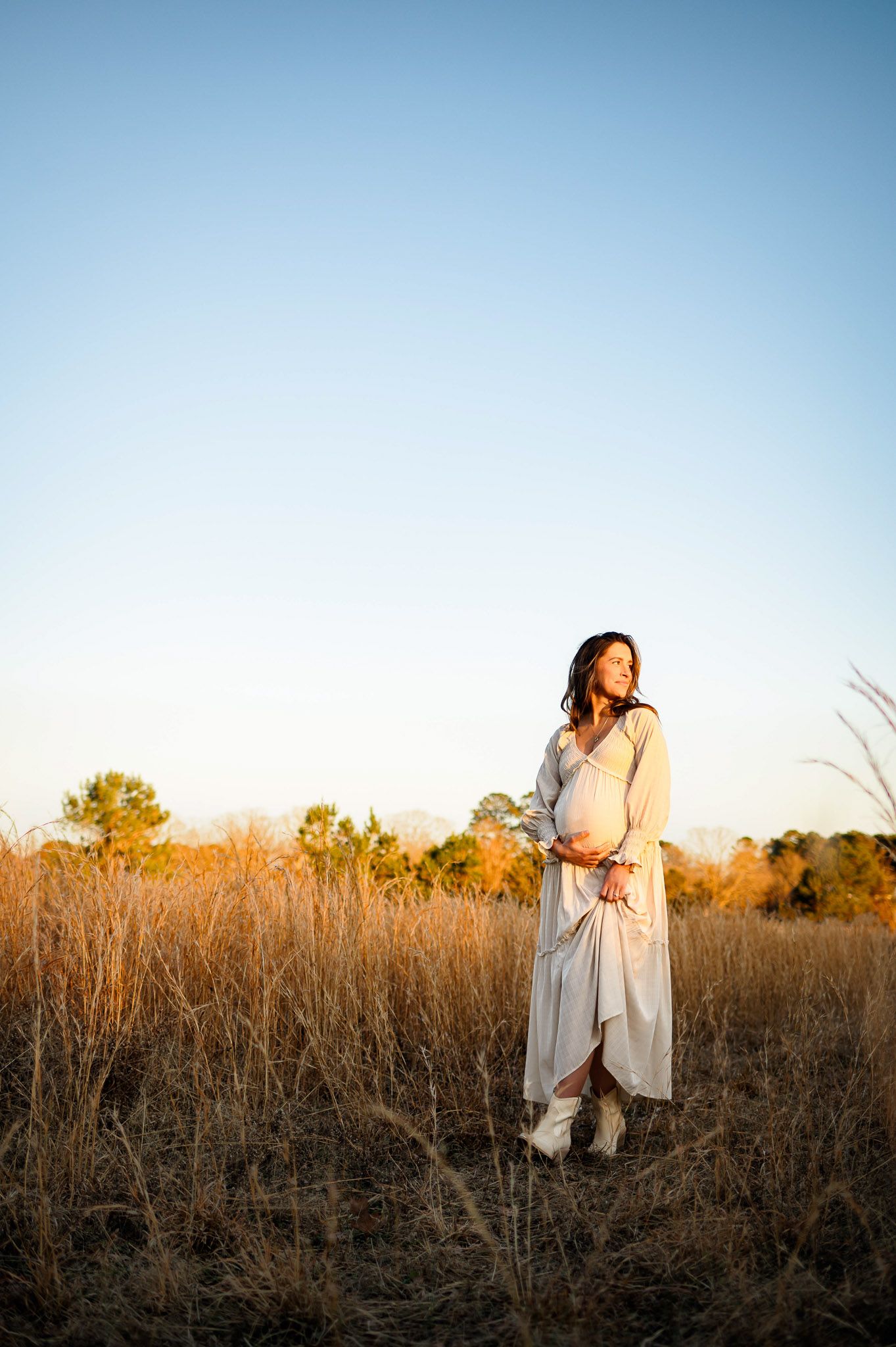 Expectant mother standing in tall grass during golden hour maternity photography session in Raleigh North Carolina