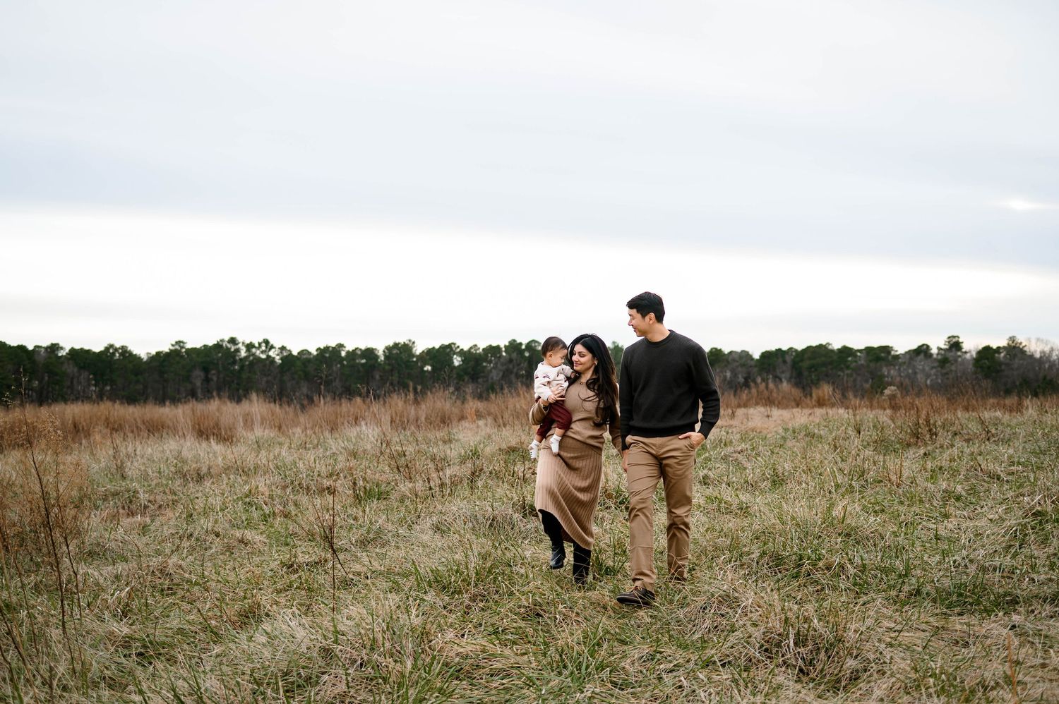 Family of three walking together through an open field during an outdoor family photography session in Raleigh North Carolina