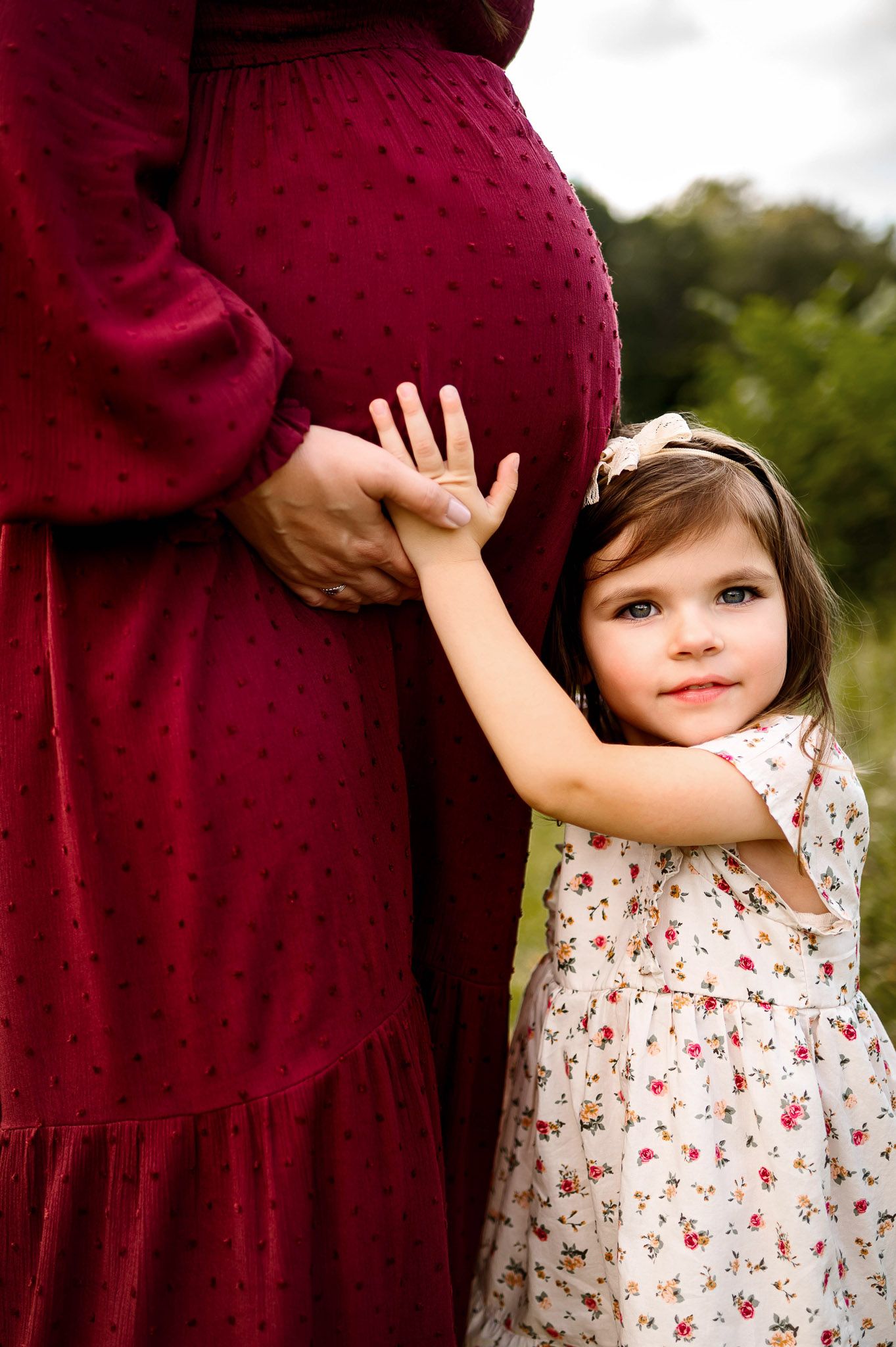 Toddler touching her mother’s pregnant belly during outdoor maternity photography session in Raleigh NC