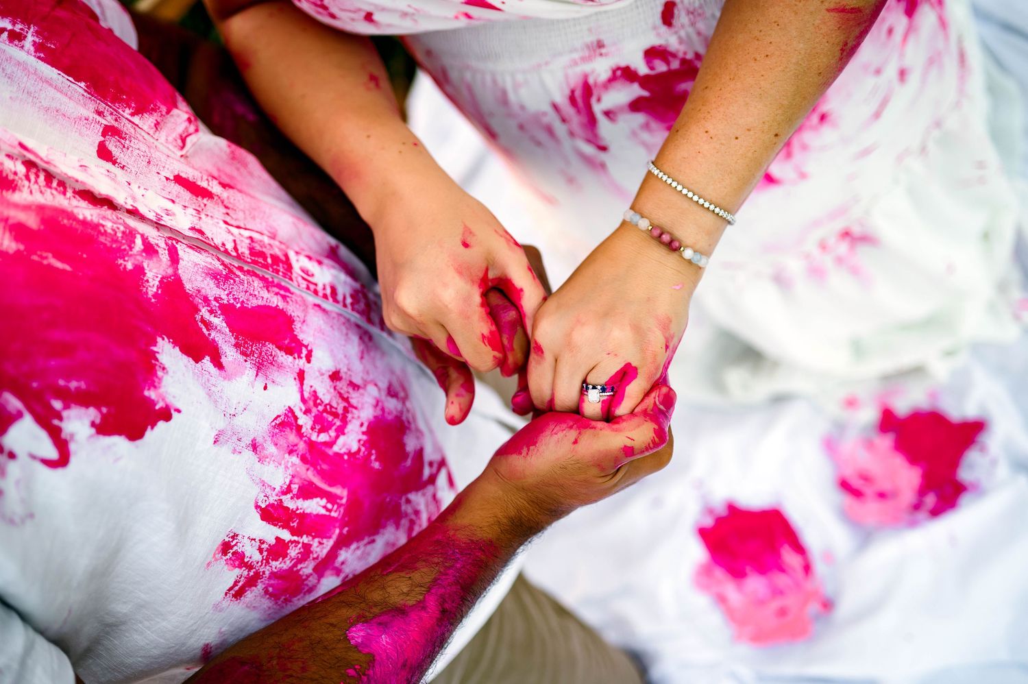 Close-up of expecting parents holding hands covered in pink paint during a gender reveal with a Raleigh NC family photographer