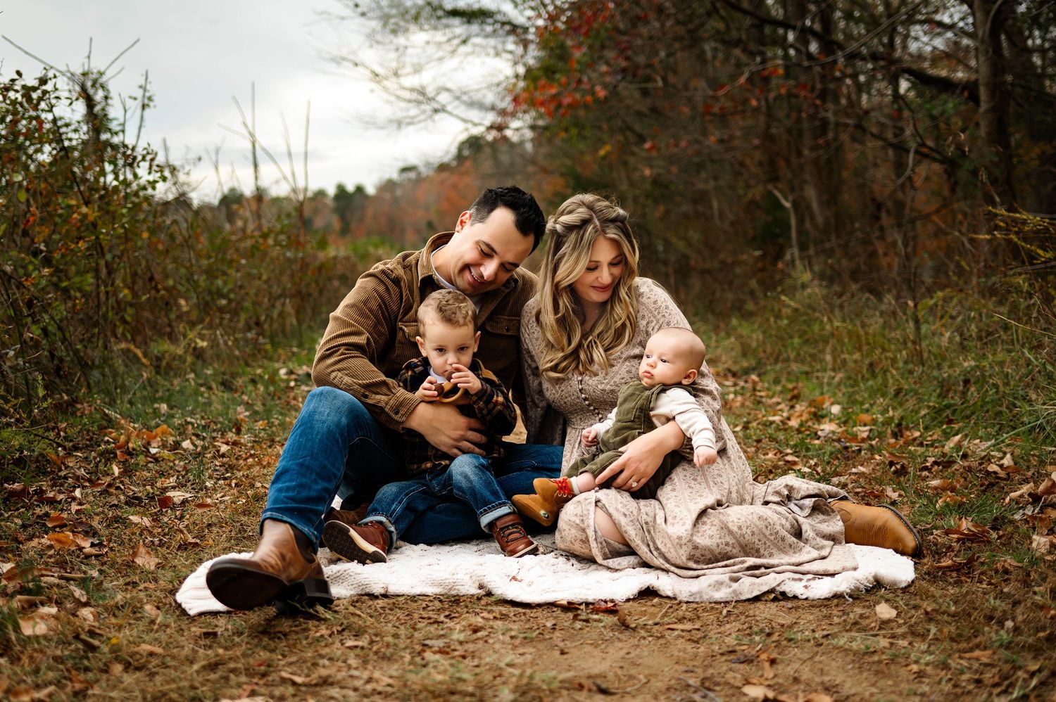 Family lying together on autumn ground reading books and enjoying quality time in nature during fall season with raleigh family photographer