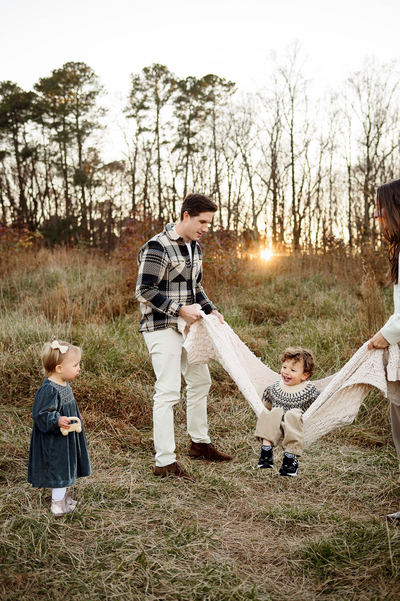 Parents swinging their young son in a blanket during a candid outdoor family photography session near Wake Forest NC