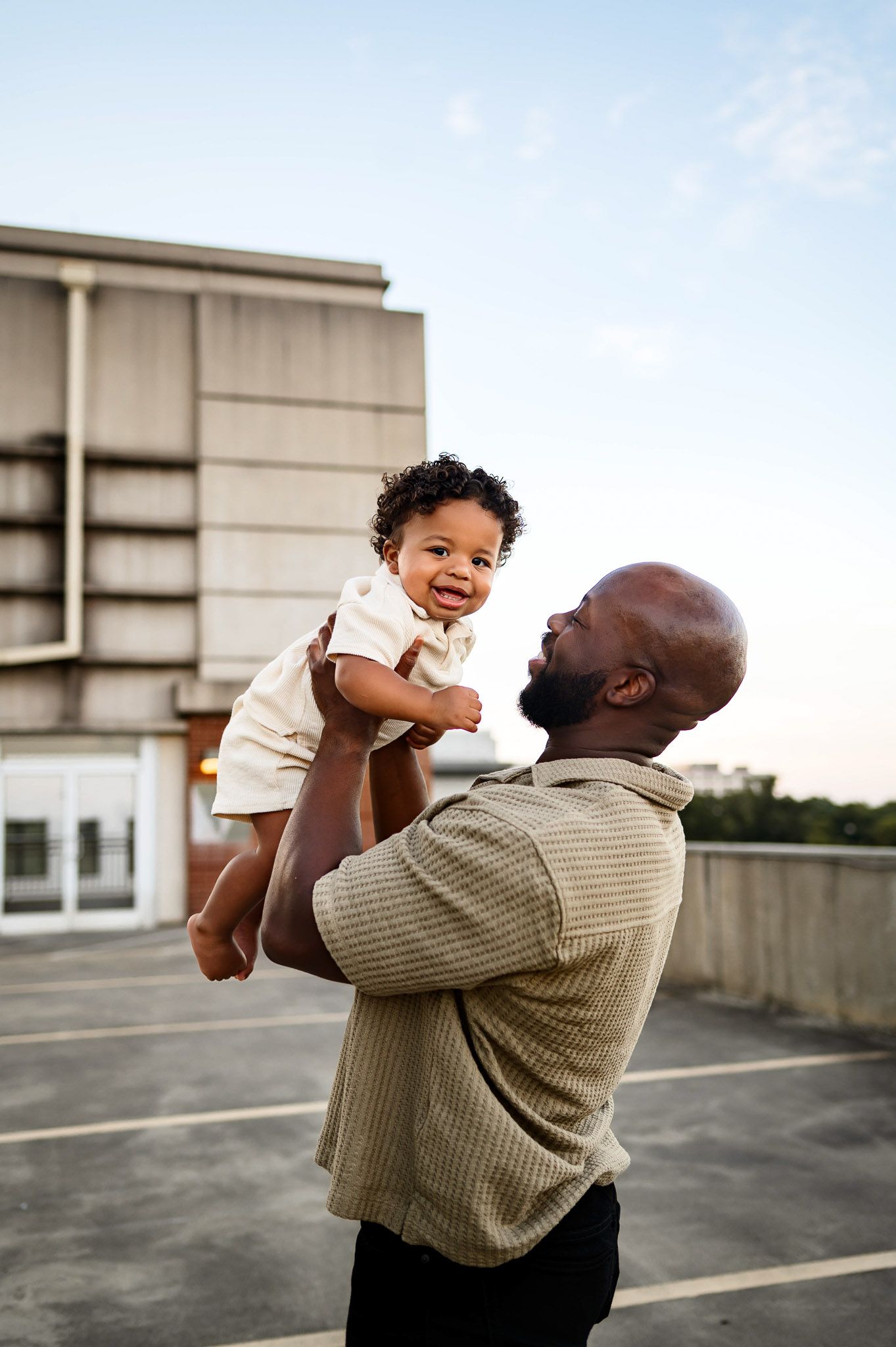 Father lifting his toddler in the air during a sunset family photography session in downtown Raleigh