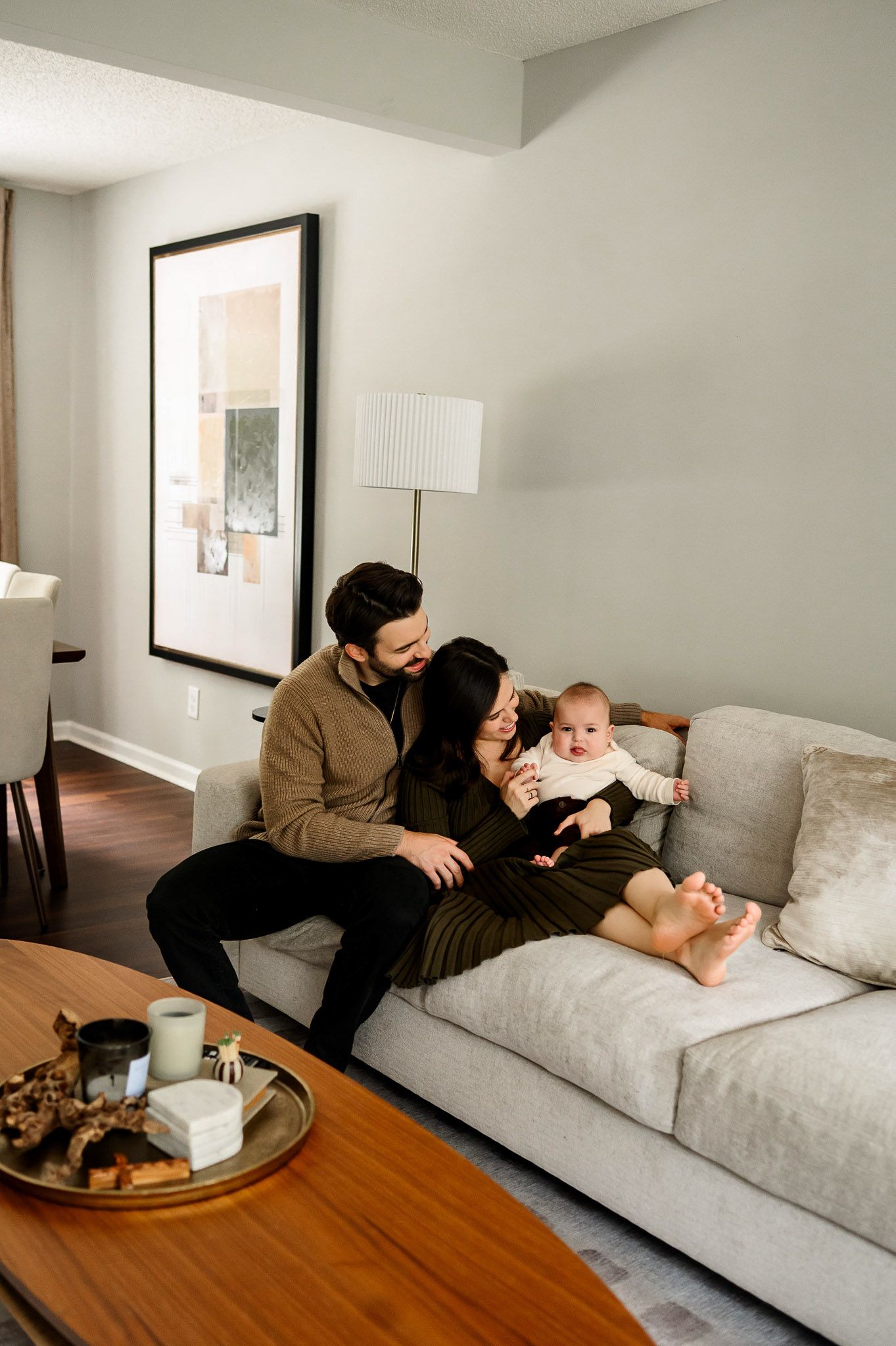 Parents sitting together on their living room couch with their baby during a lifestyle family photography session in Raleigh, North Carolina