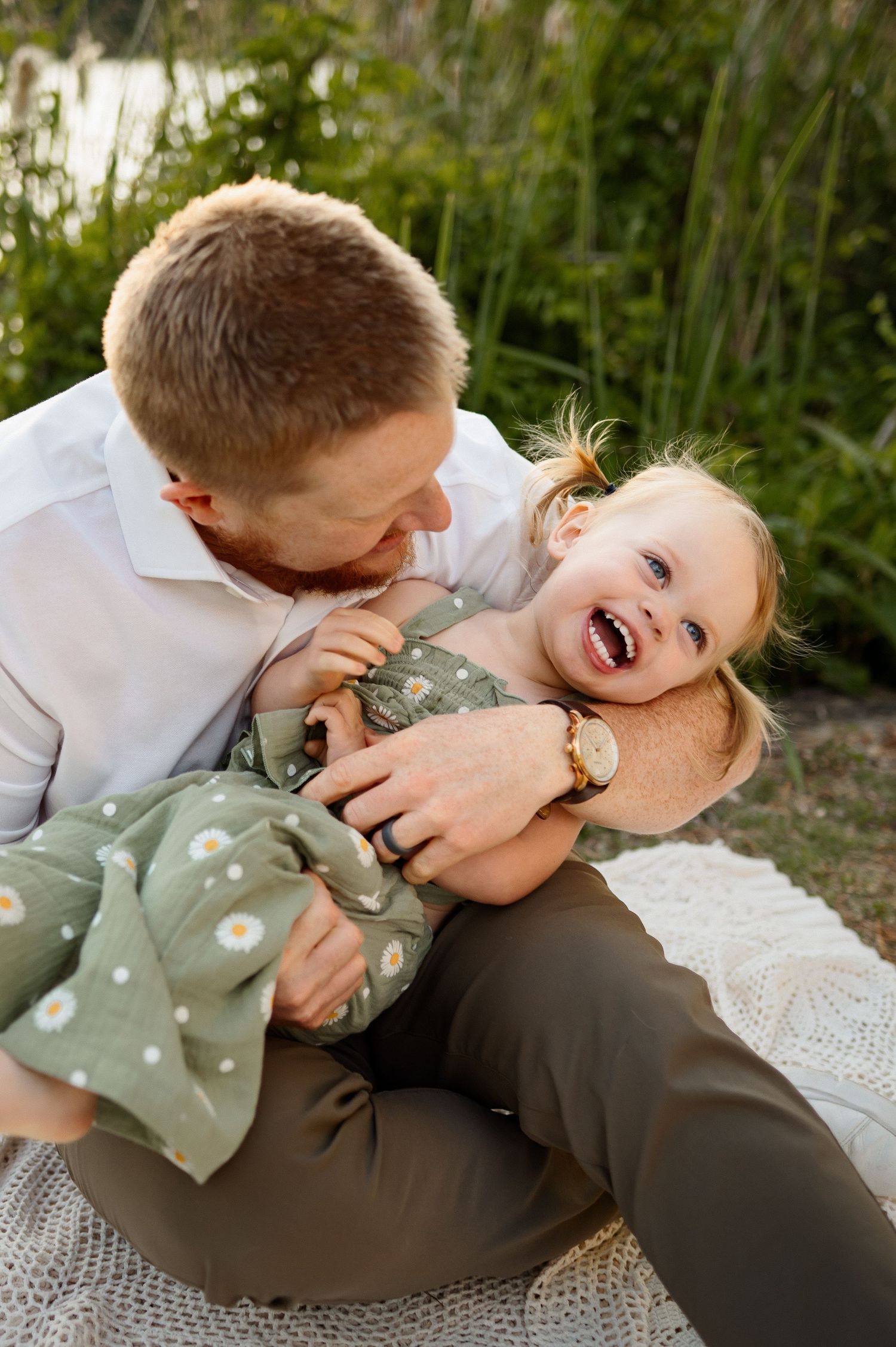 Toddler girl laughing while being tickled by her father during a relaxed outdoor family photography session in Raleigh