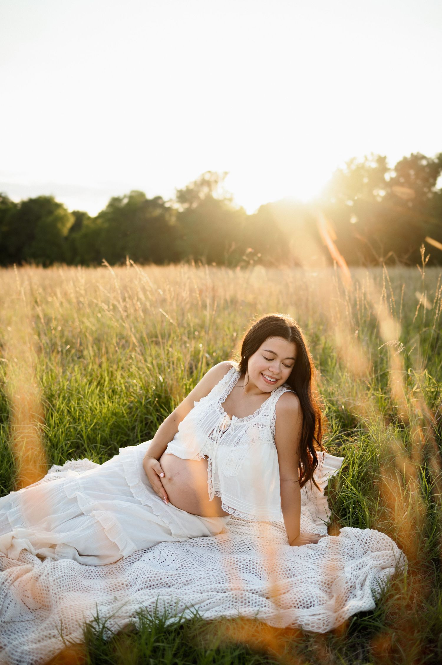 Mother sits alone in a field of tall grass during a maternity photography session during golden hour in Raleigh NC